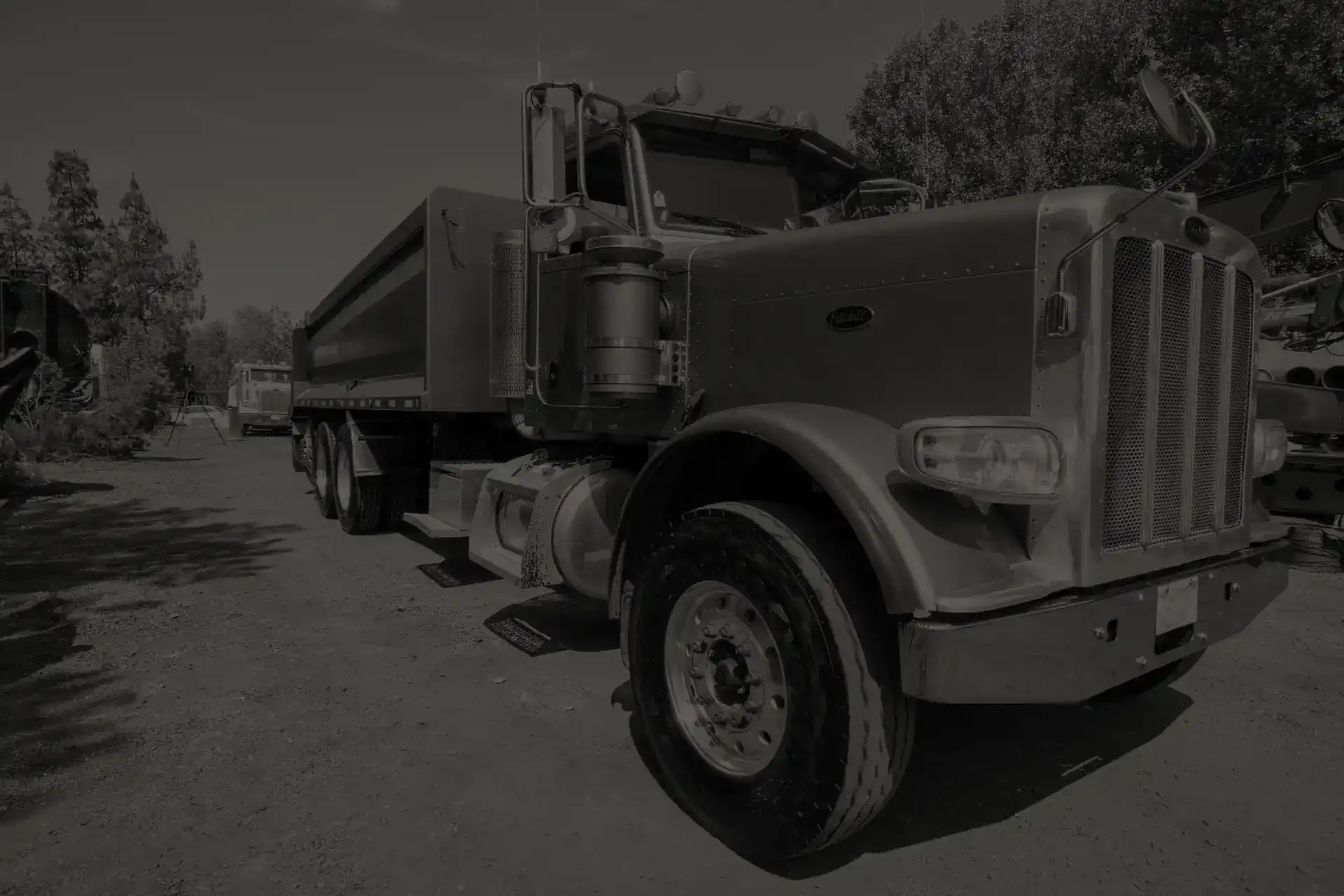 Front and side view of a large commercial dump truck parked in aa dirt lot in San Diego path near trees.