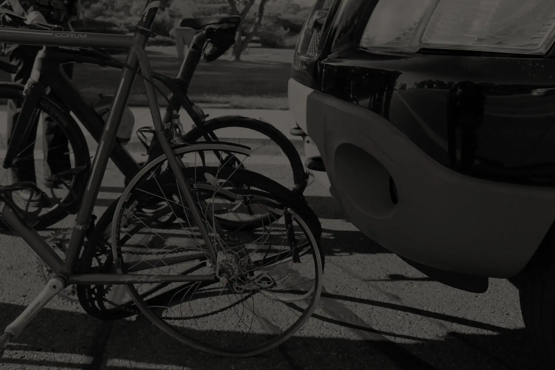 Damaged bicycle with bent front wheel next to the front bumper of a black vehicle parked on asphalt.