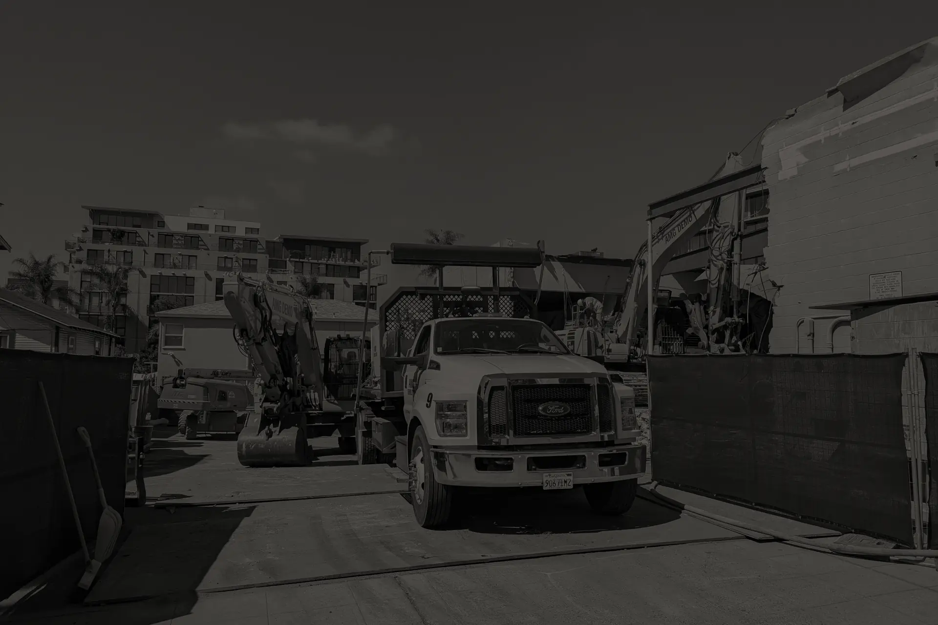 Construction site with a white Ford truck and excavators near buildings under clear sky in San Diego.