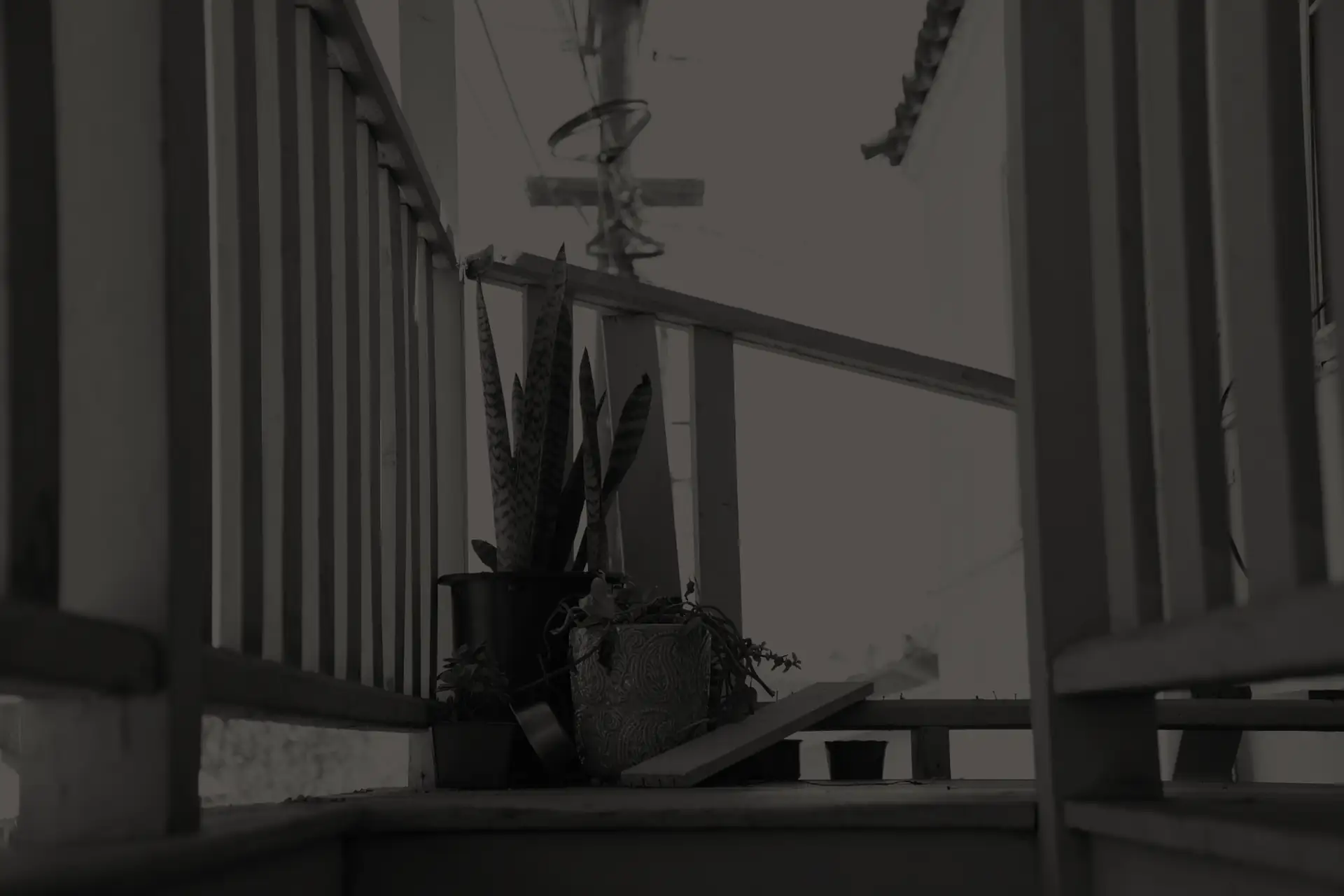 Dark apartment balcony with potted plants and broken wood railings.