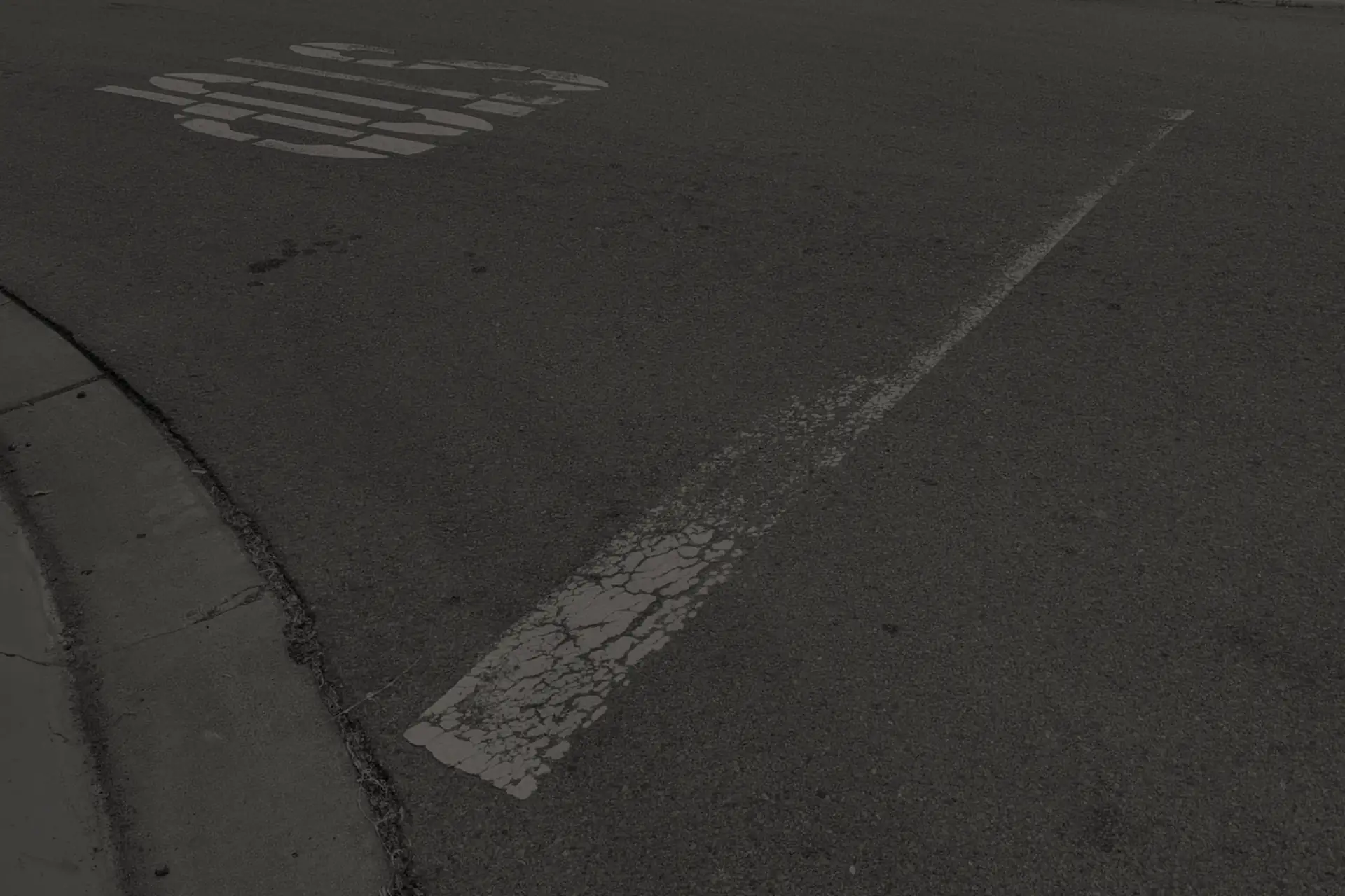 Worn white lane line and faded 'STOP' marking on dark asphalt near a concrete curb.