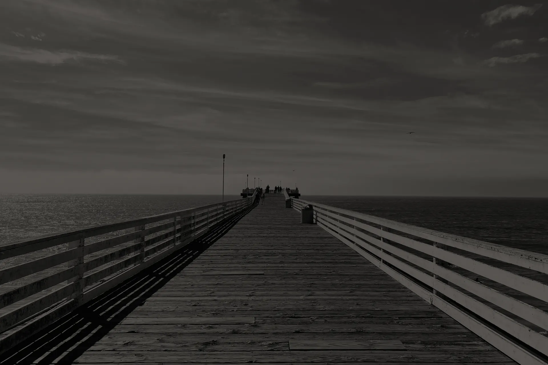 Pacific Beach Crystal Pier extending into the ocean with a few people at the far end under a cloudy sky.