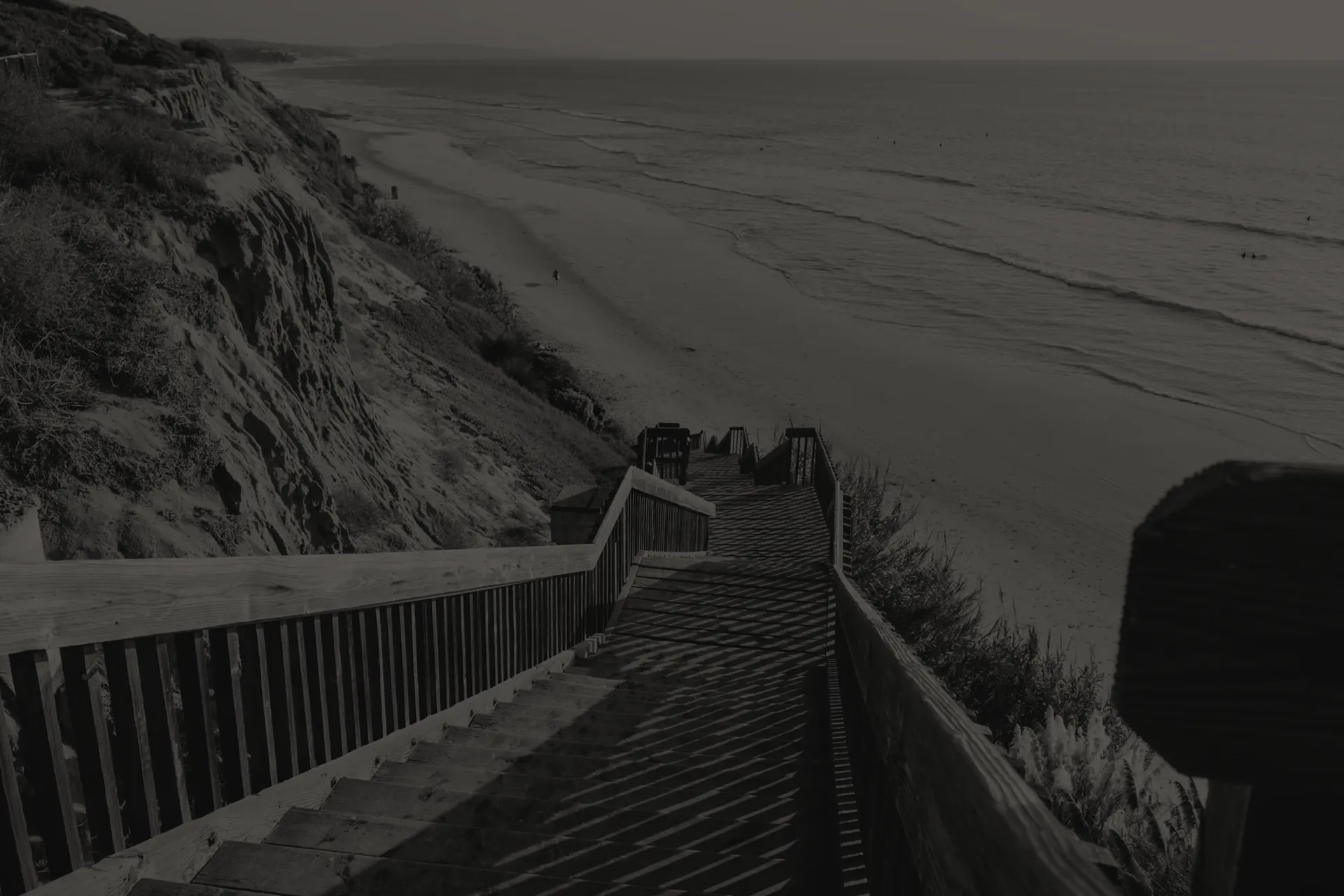 Wooden stairs descending from Encinitas cliffs to a sandy beach with ocean waves in the distance.