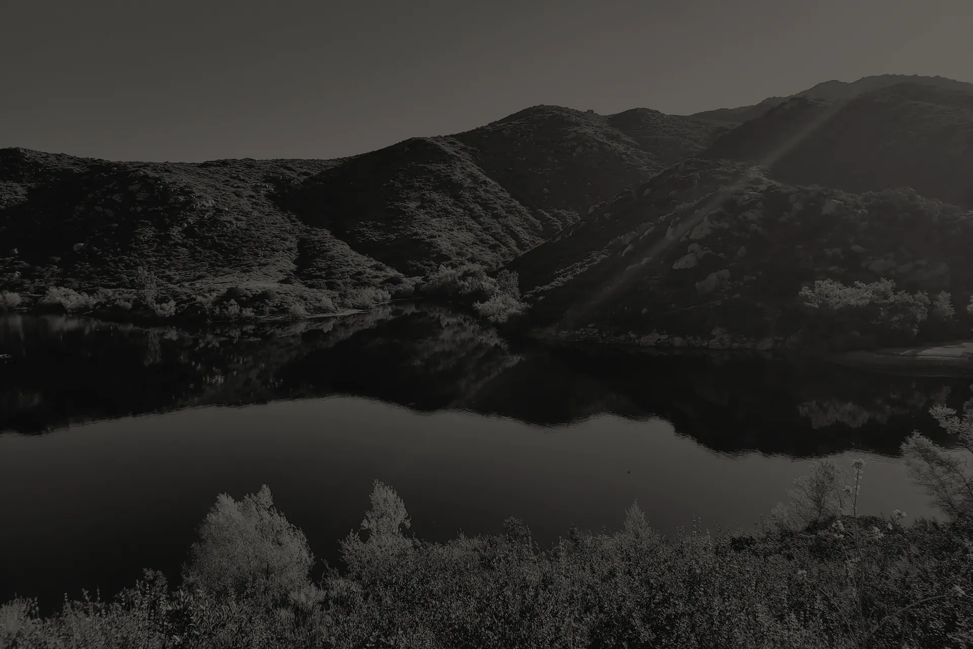Poway lake reflecting surrounding hills and vegetation under a clear sky at sunset.