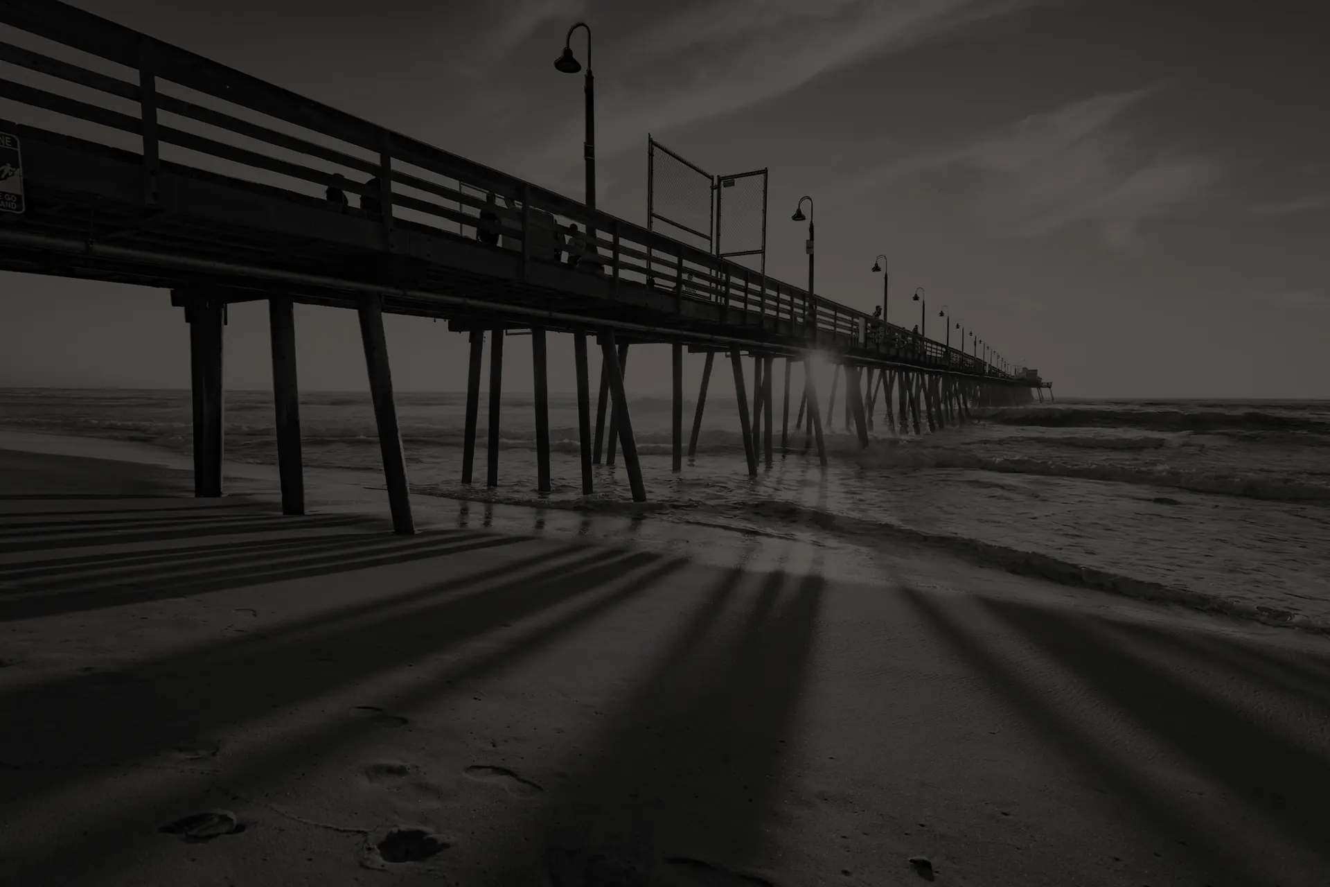 Imperial Beach wooden pier extending over ocean waves at sunset with shadows cast on sandy beach.
