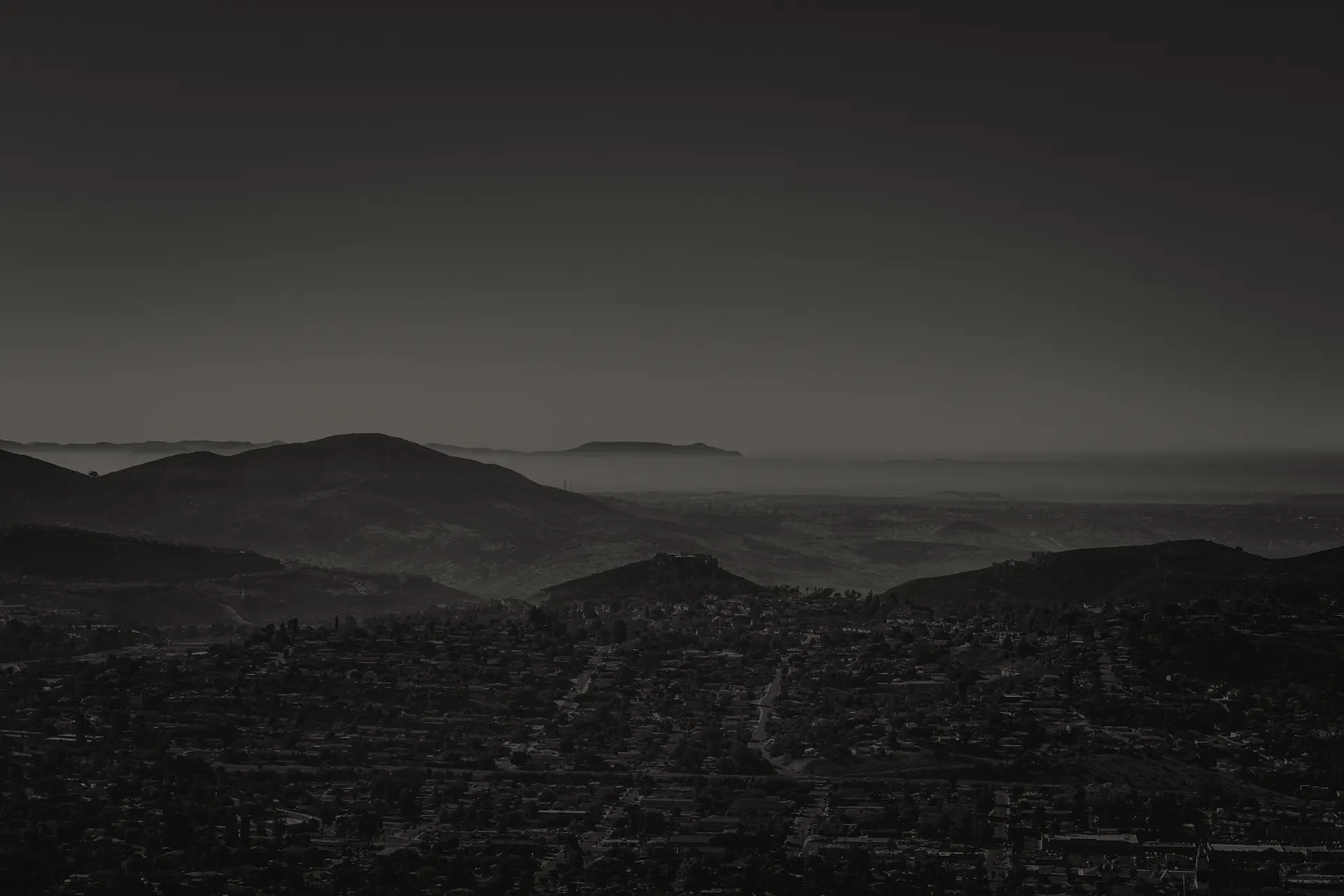 Dark-toned panoramic view of El Cajon valley with hills and scattered buildings under a gradient sky.