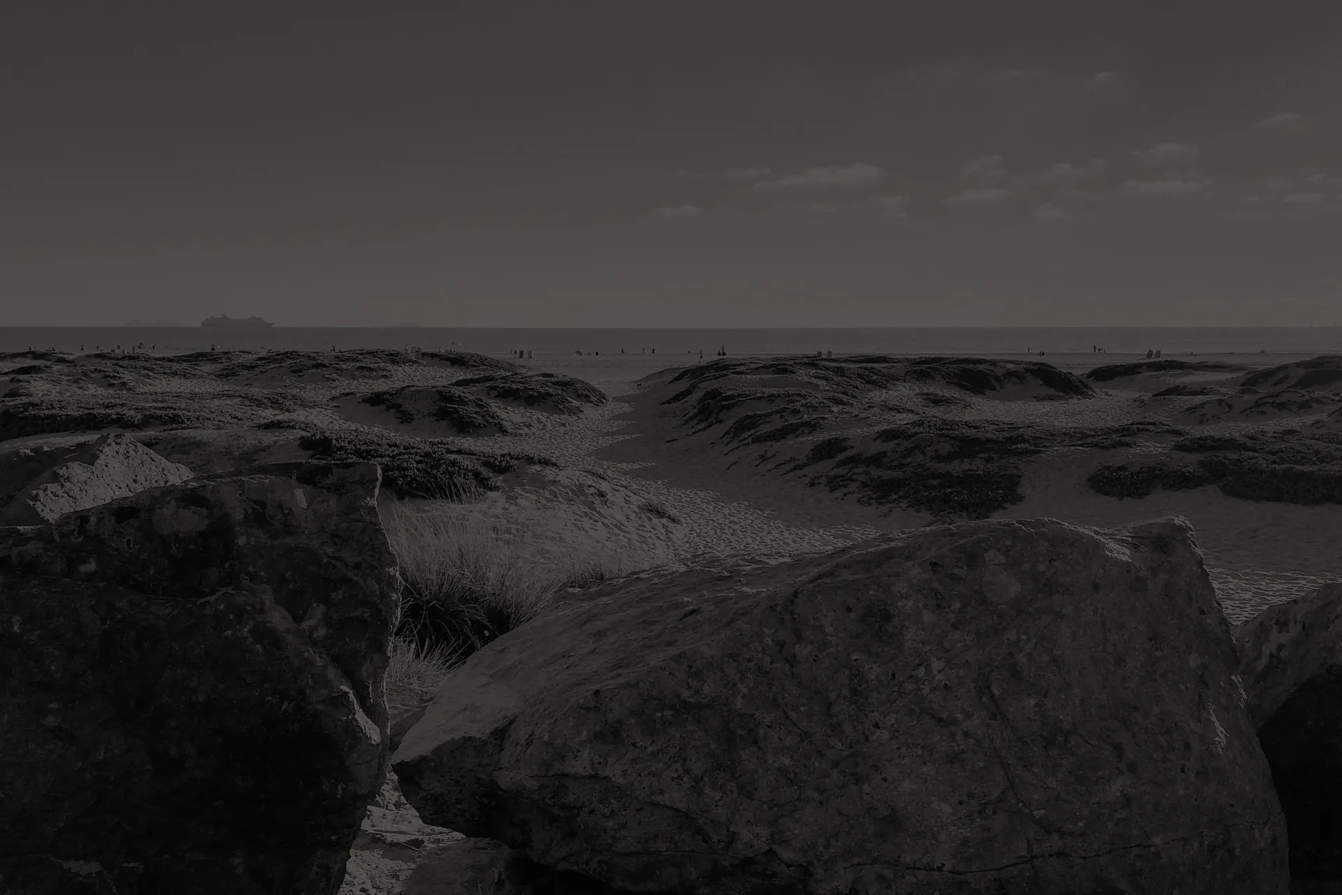 Coronado sandy beach dunes with large rocks in foreground and calm ocean horizon in the distance.