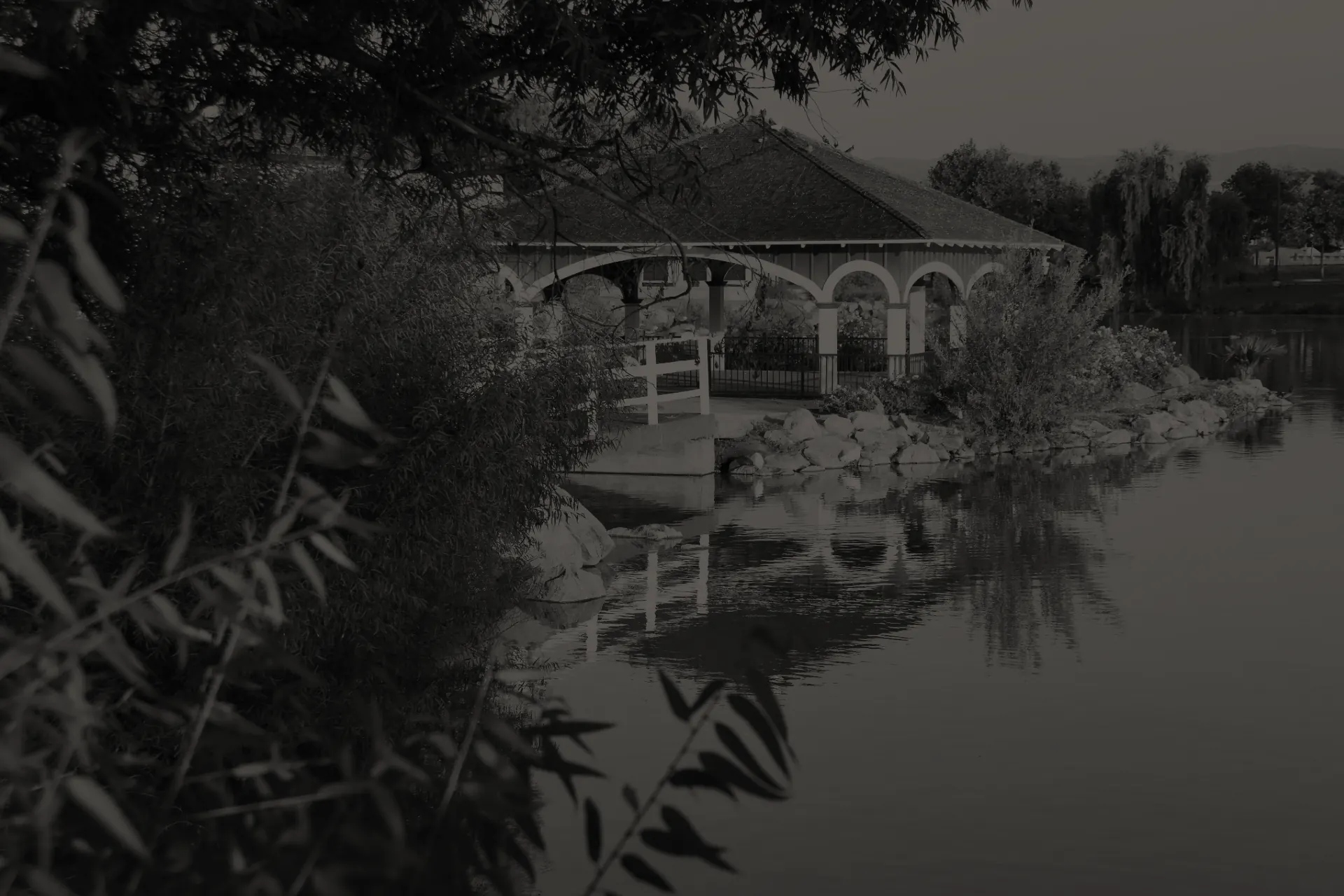Historic Lakeside Lindo Lake boathouse-gazebo with arches by a lakeside surrounded by trees and plants with water reflections.