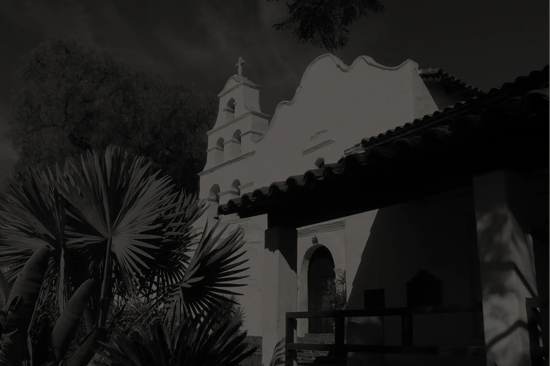 Mission San Diego de Alcalá in Mission Valley with its white bell tower, red tile roof, and fan palms in the foreground.