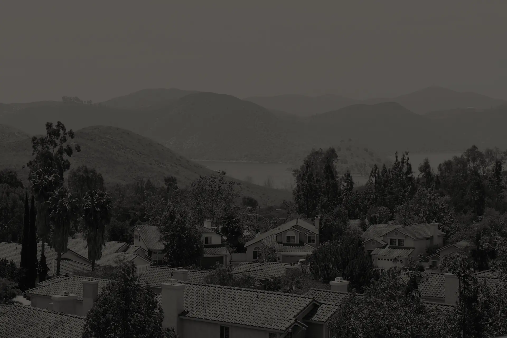 Escondido neighborhood with tile-roof houses, trees, hills, and a reservoir in the background.