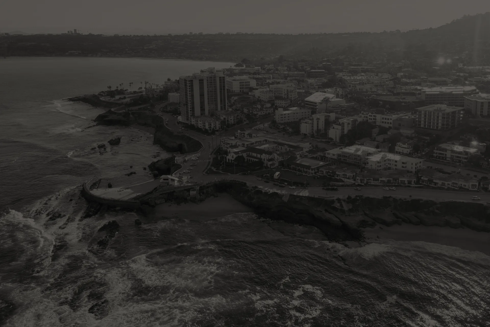 Aerial view of La Jolla coastline with rocky shore, ocean waves, and buildings near the beach.