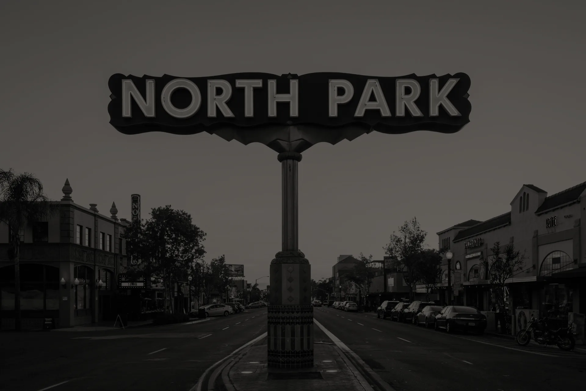 Street view with a tall sign reading 'NORTH PARK' at the center of a road dividing two rows of buildings.