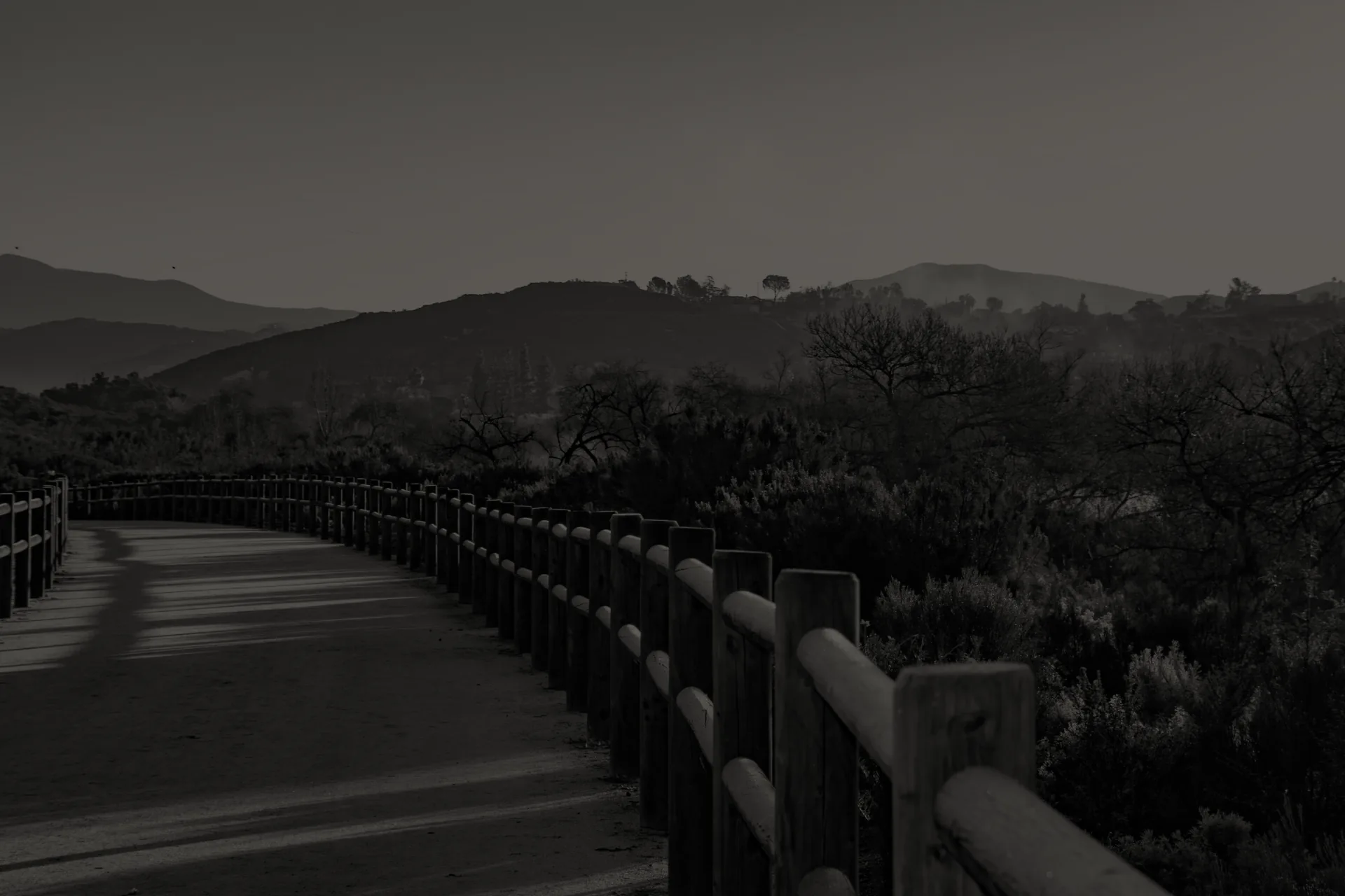 Santee Walker Preserve Trail wooden fence along a dirt trail with hills and leafless trees in the background at dusk.