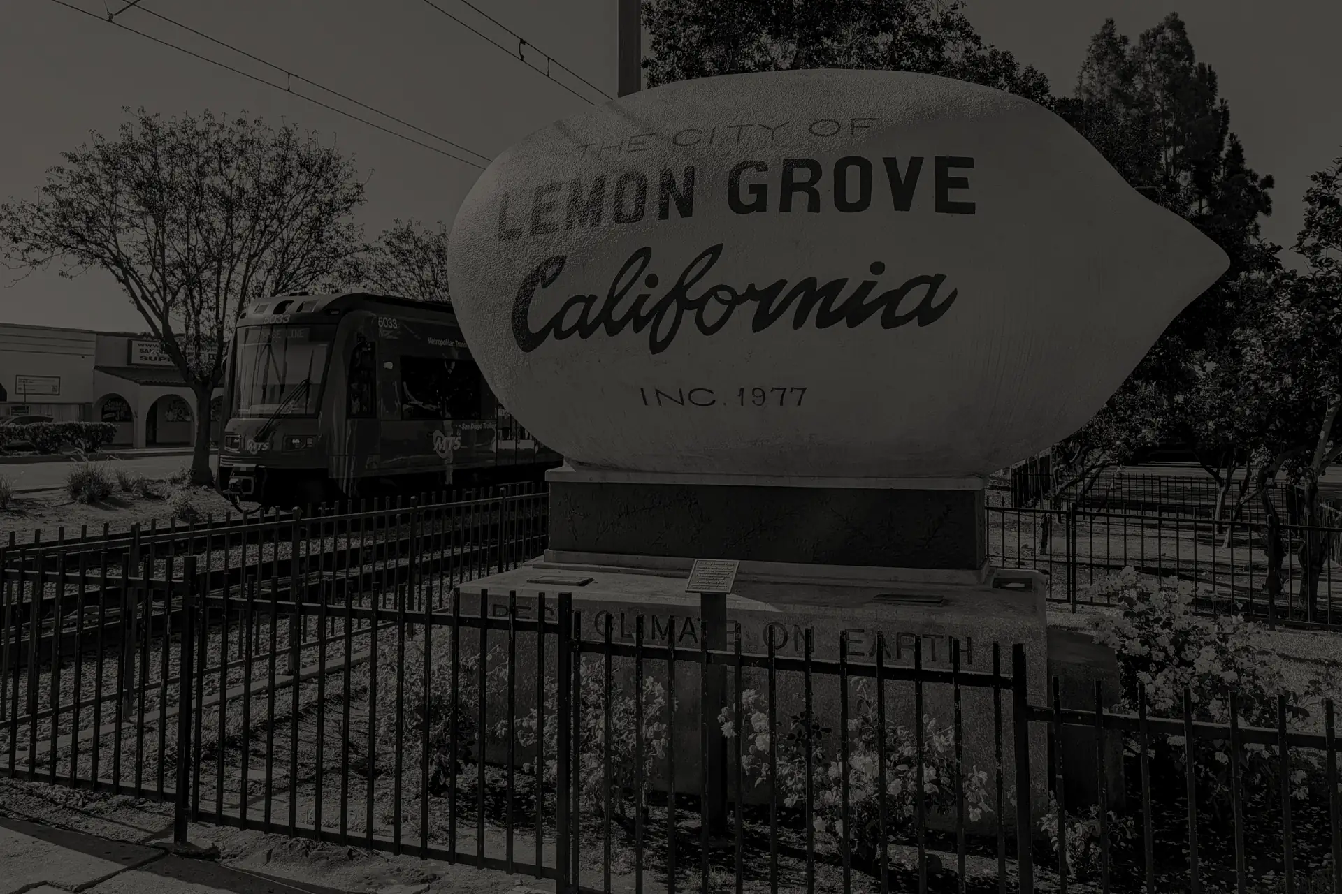 Large lemon monument reading The City of Lemon Grove California with a trolley in the background in Lemon Grove, California.