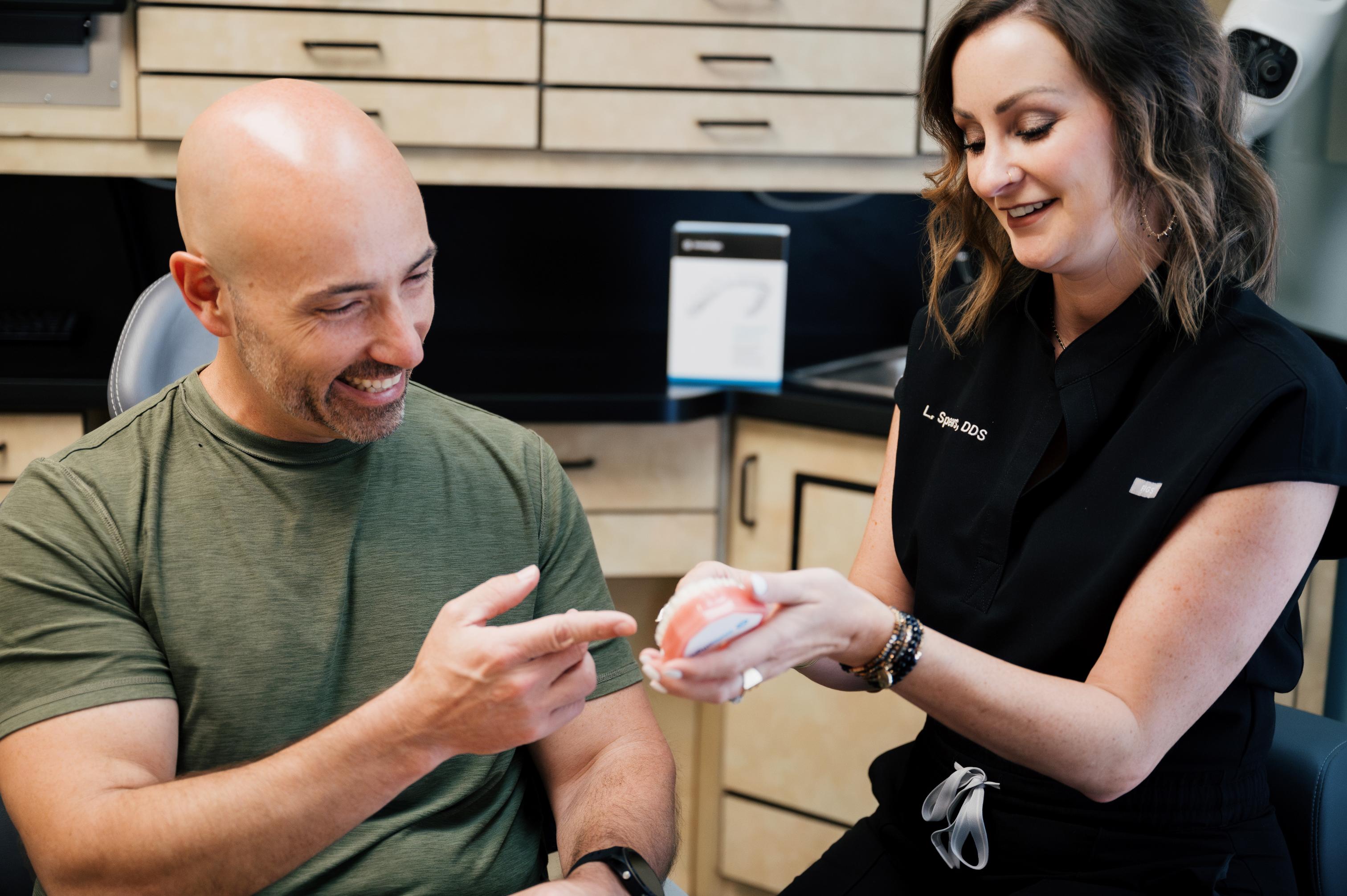 Male patient smiles during dental consultation with model teeth at Carolina Crossroads Dental Care