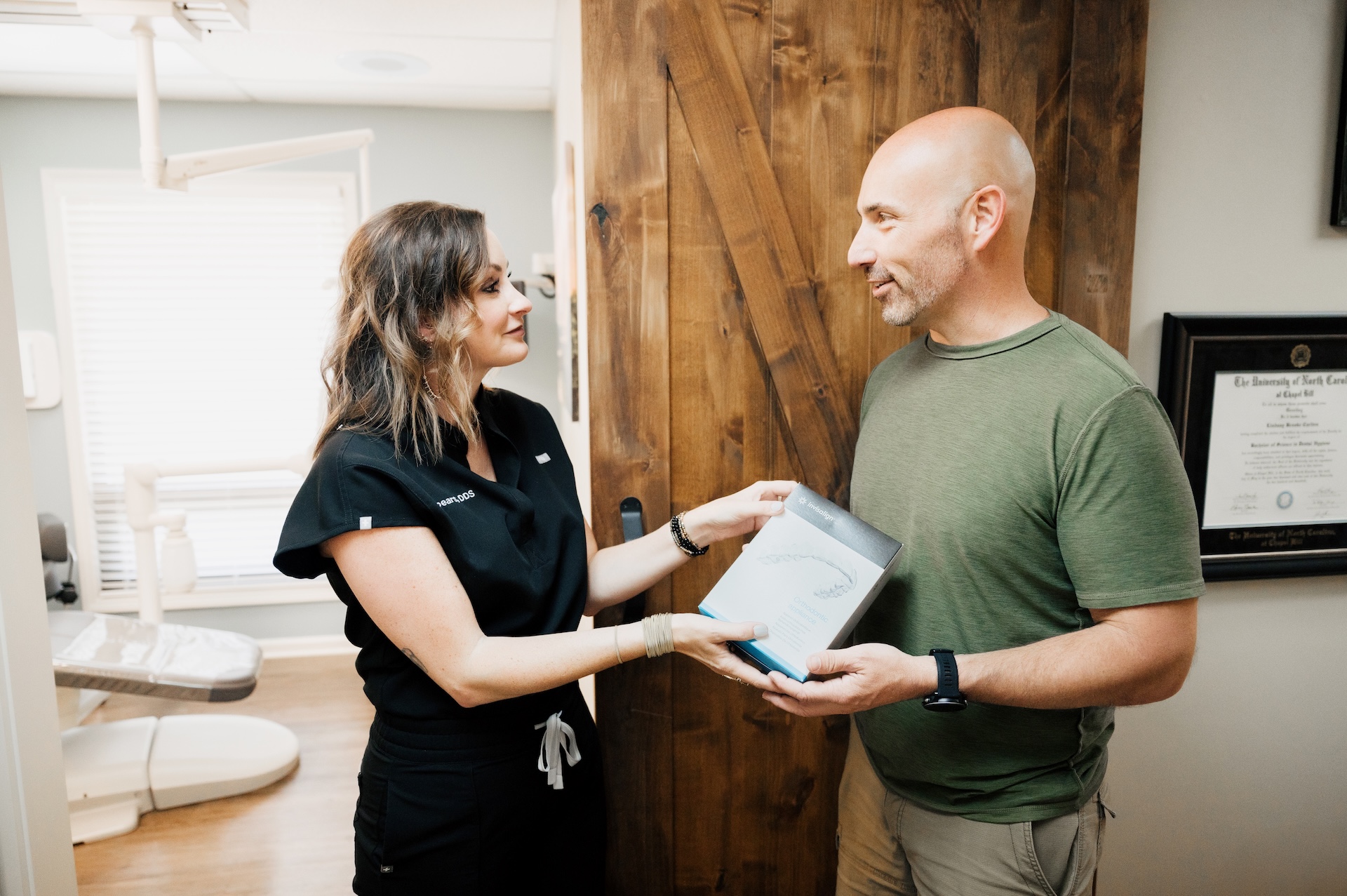 Dentist at Carolina Crossroads handing adult male client his invisalign sets