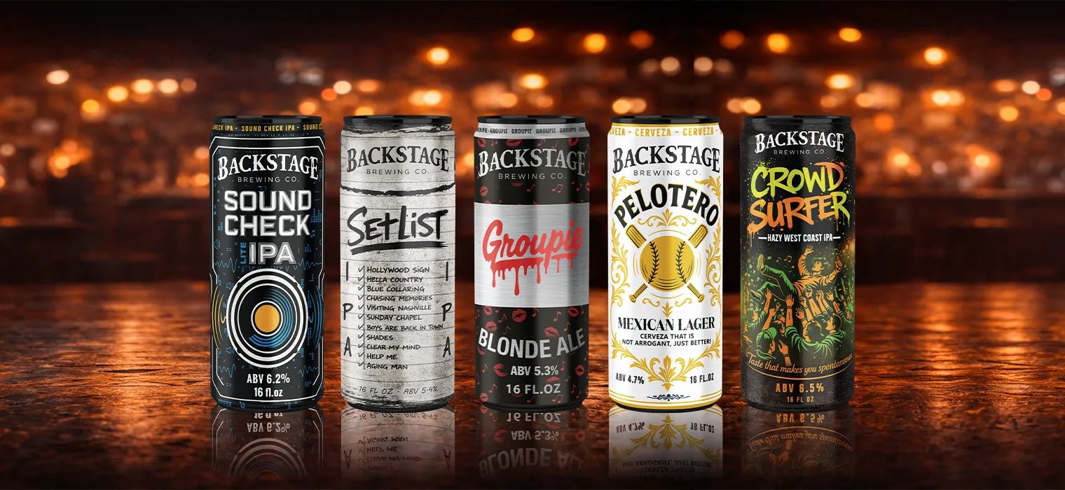 Five Backstage Brewing Co. beer cans lined up on a reflective surface with a blurred warm light background; from left to right: Sound Check IPA, Set List with a handwritten song list, Groupie Blonde Ale with red lips and music notes, Pelotero Mexican Lager with baseball design, and Crowd Surfer Hazy West Coast IPA featuring a crowd surfing illustration.