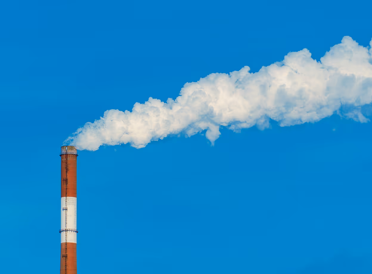 Industrieller Schornstein mit weißem Rauch vor blauem Himmel als Symbol für Raucherpausen während der Arbeitszeit im Betrieb.