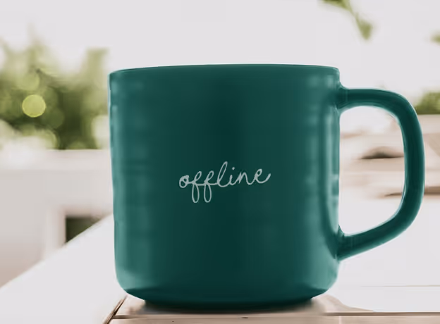 Grüne Kaffeetasse mit Aufschrift offline auf Holztisch. Symbol für gesetzliche Pausenzeiten im Arbeitsalltag.