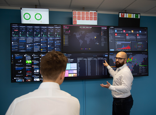 Thomas Edelmann (CTA bei agilimo) zeigt Mitarbeiter IT-Infrastruktur an großen Monitoren.