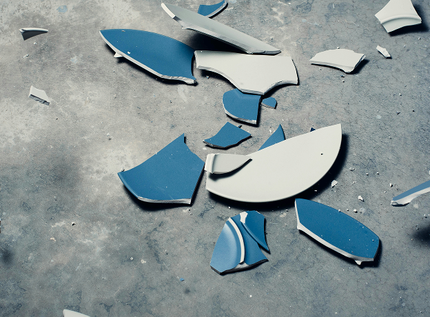 Zerbrochene blaue Keramikscherben auf grauem Betonboden symbolisieren das Scheitern strategischer Projekte durch fehlende Struktur.