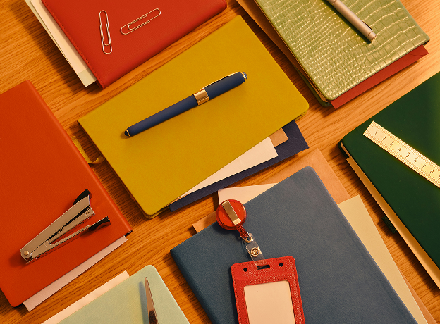Bunte Notizbücher, Stift und Büromaterialien auf Holztisch – symbolisieren strukturiertes Task Management im Projektalltag.