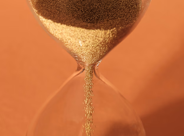Sanduhr mit rieselndem goldenen Sand als Sinnbild für ablaufende Fristen bei der Zeiterfassungspflicht 2026.