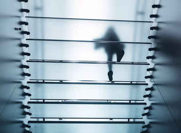 Person geht über eine Glasbrücke mit metallischen Streben – Metapher für transparente und riskante Strukturen in der Retainer-Abrechnung.