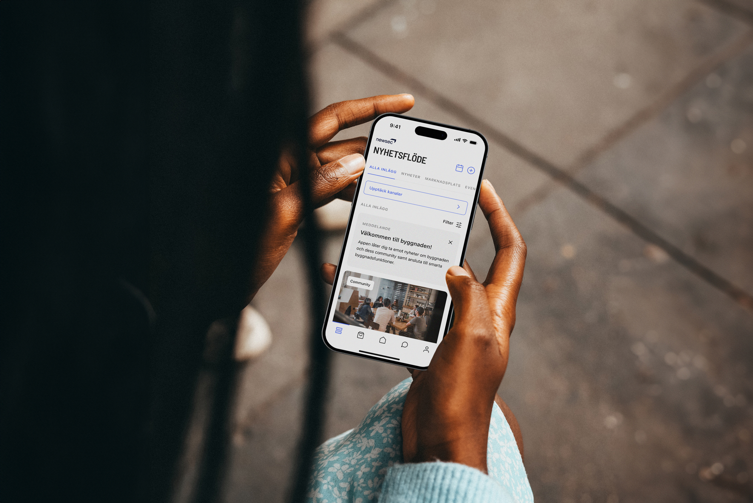 Woman holding phone displaying the Spaceflow tenant app newsfeed in Swedish language