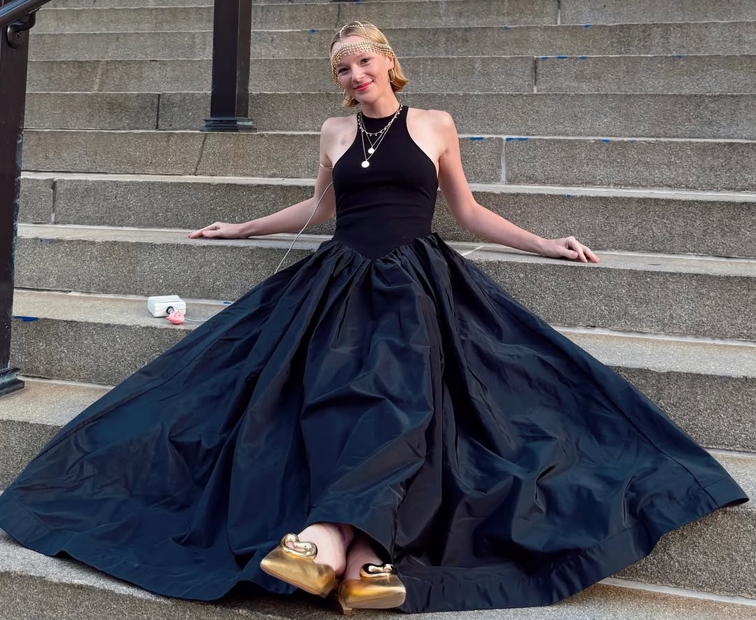 Woman in a long black gown sitting on outdoor steps and smiling.