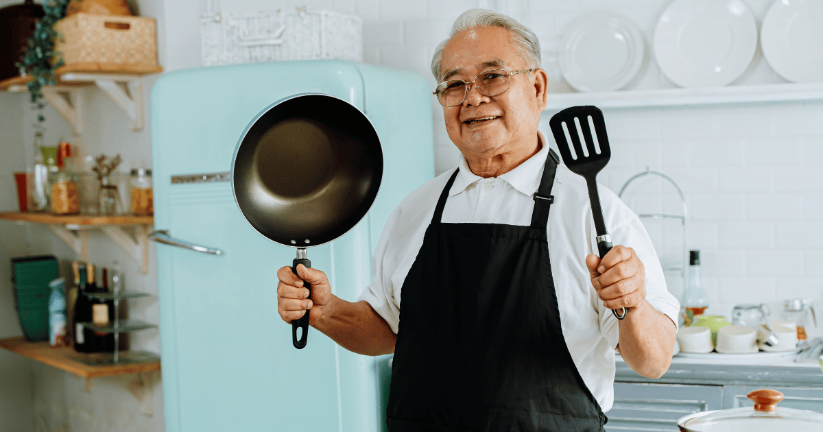 An older man holding up a pan and a spatula