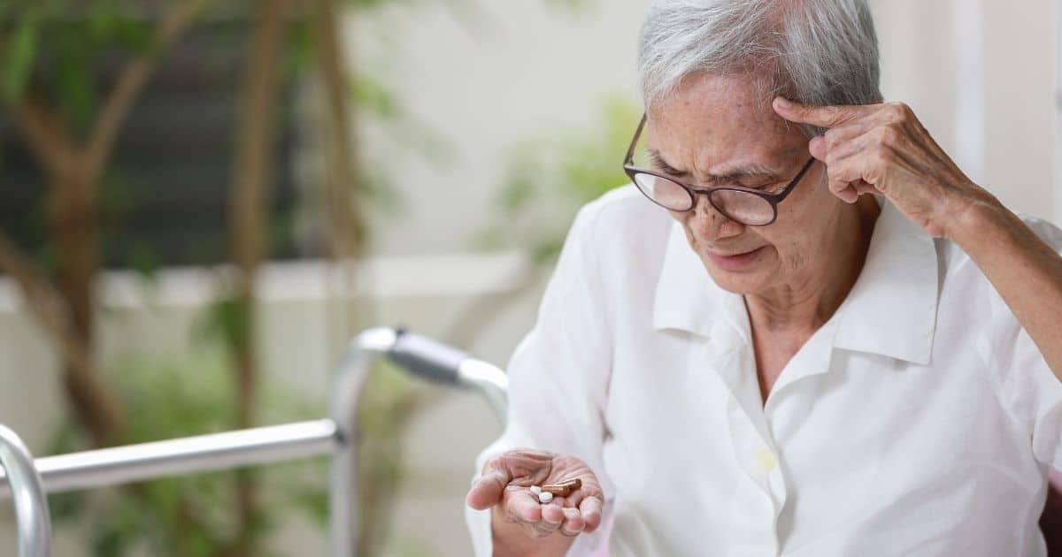 An elderly person looking at pills whilst appearing confused 