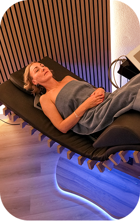 Frau entspannt auf relounge Regenerationsliege im warmen Wellnessraum – EMS-Wärmetherapie für tiefe Muskelentspannung und smarte Erholung.