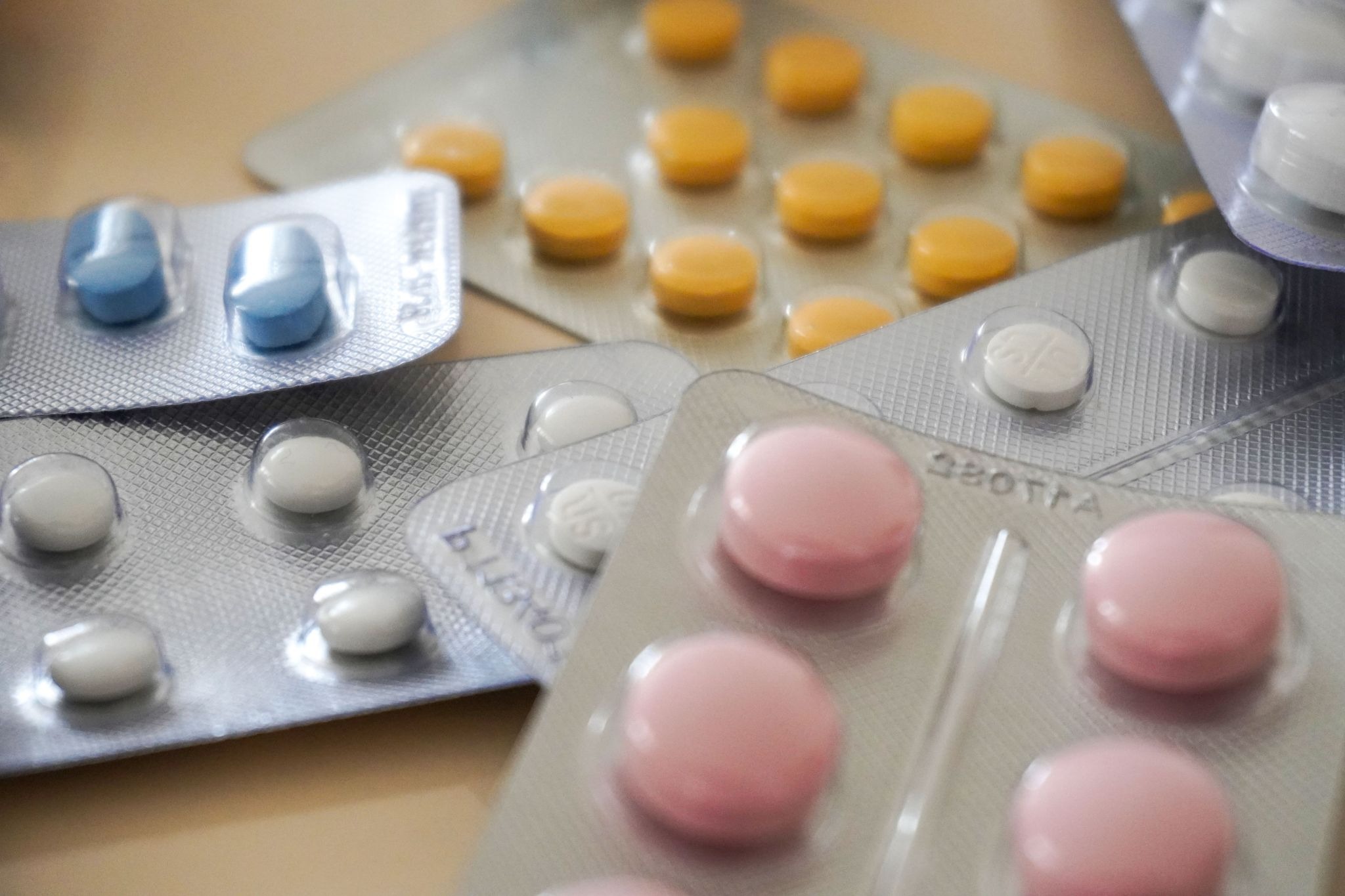 Close-up view of multiple silver blister packs containing various prescription pills and tablets, including round pink, yellow, blue, and white medications.