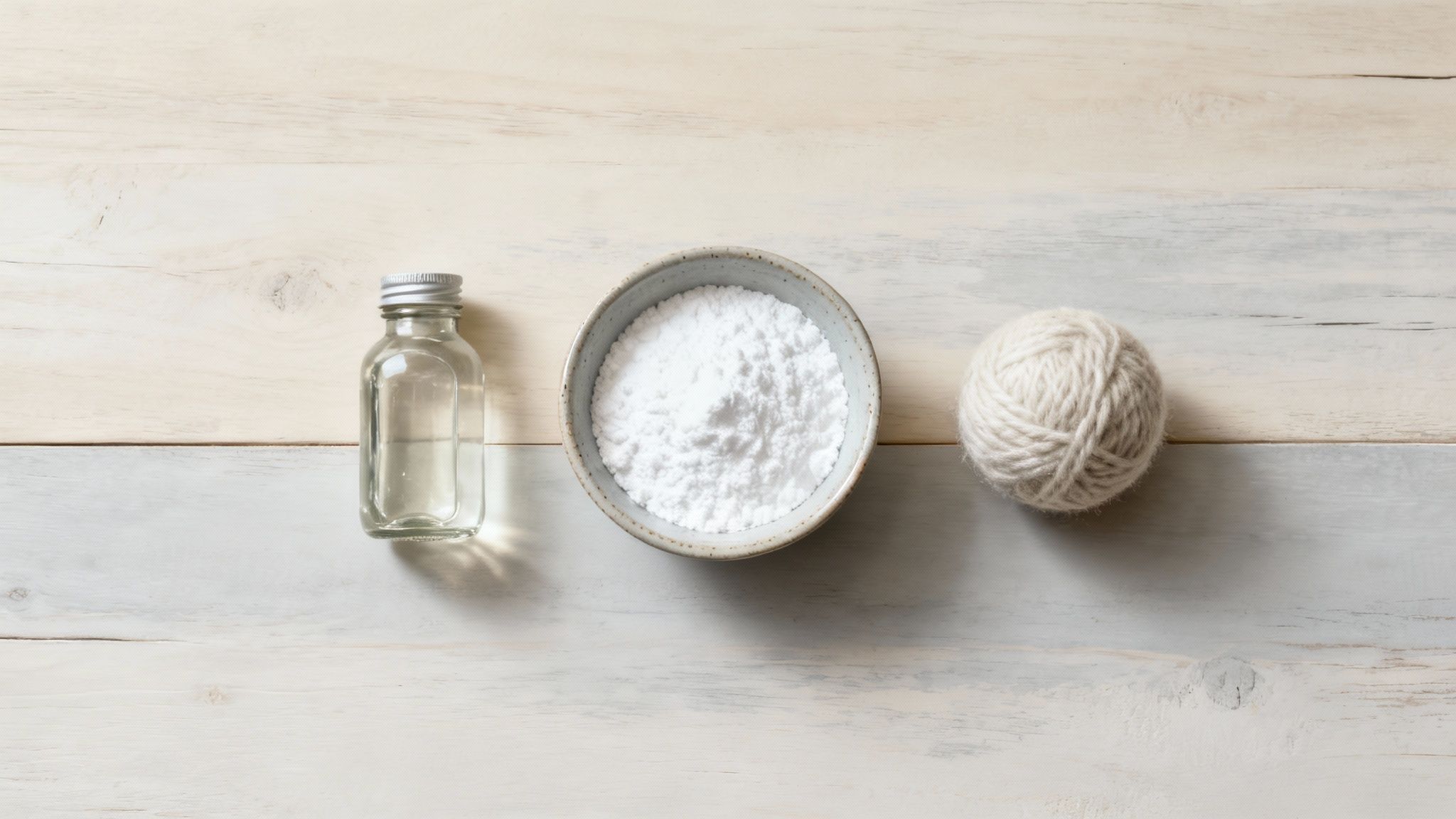 A bottle of white vinegar and a bowl of baking soda next to a stack of clean laundry