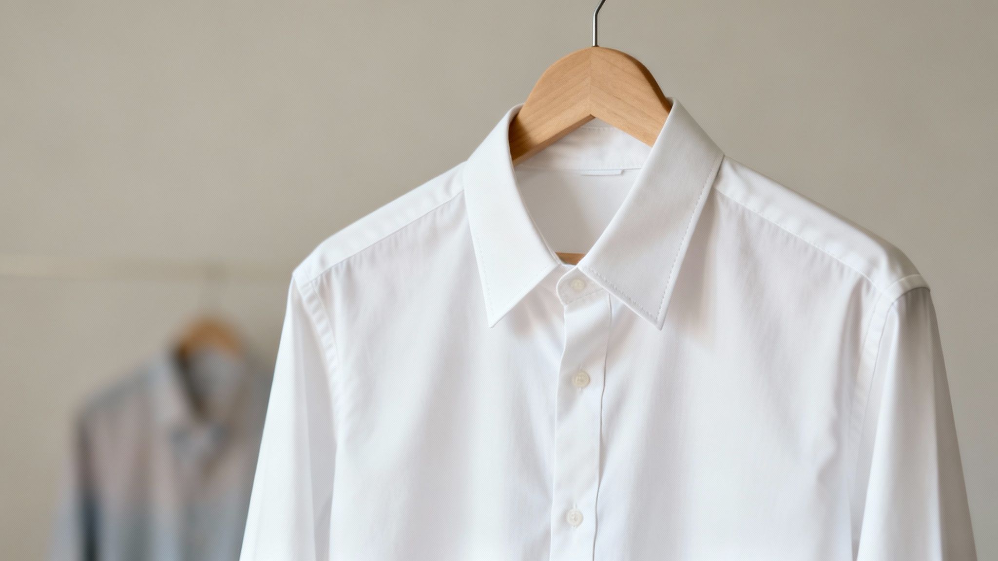 A pristine white dress shirt hangs neatly on a wooden hanger, ready to wear.