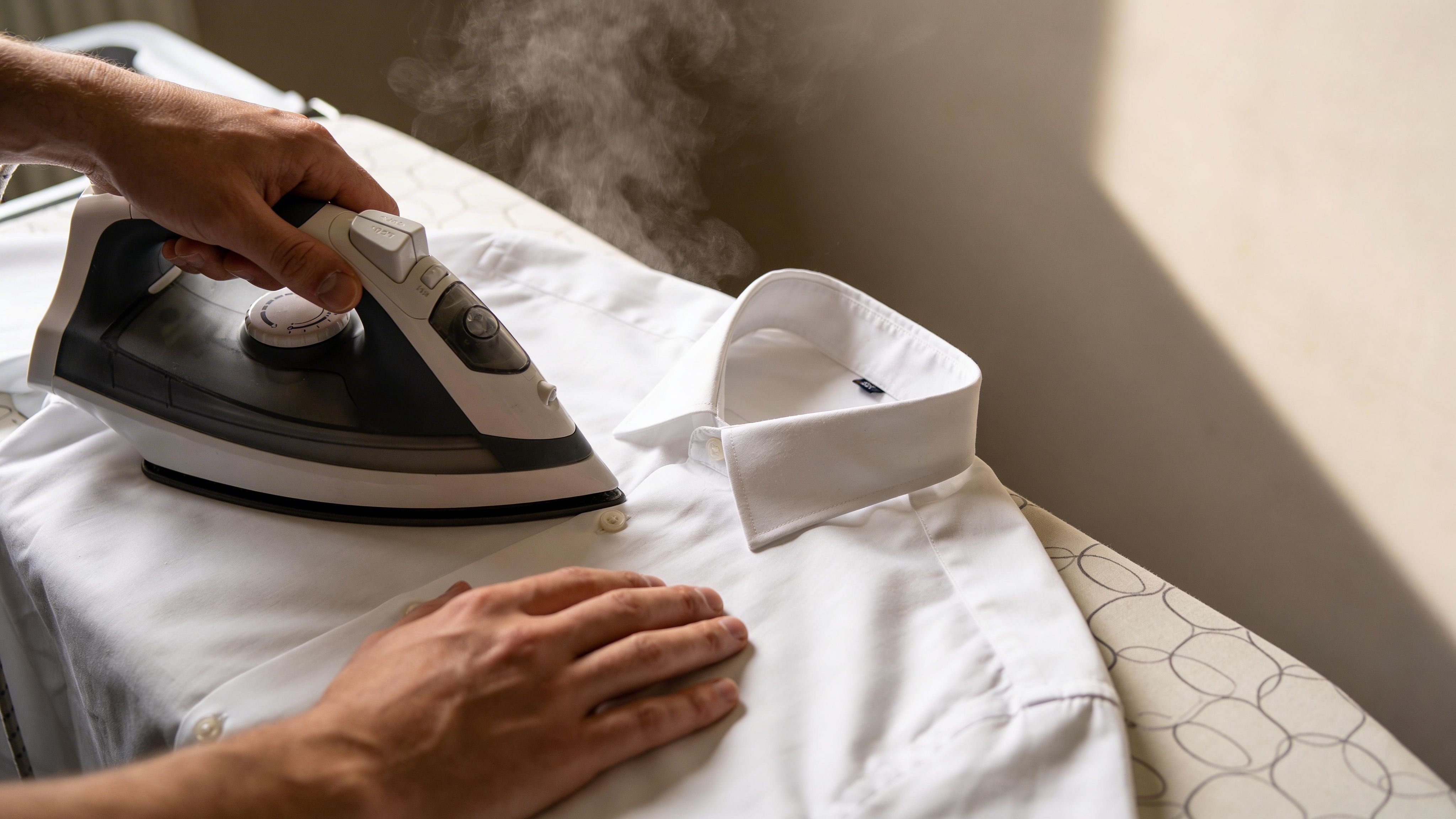 A person carefully ironing a crisp white dress shirt on an ironing board using a steam iron.