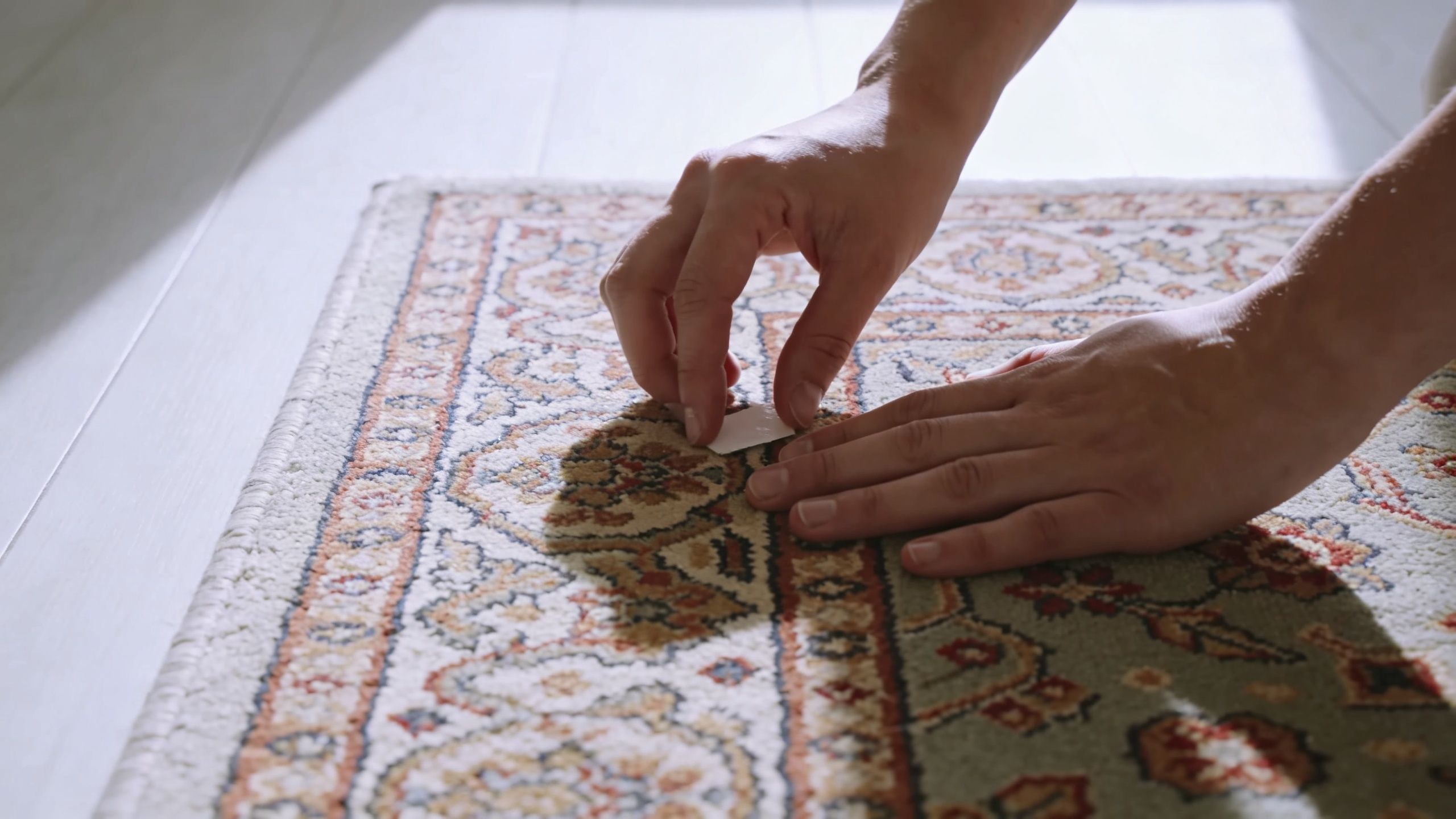 A pair of hands carefully applies a small adhesive patch to a decorative Persian style rug.