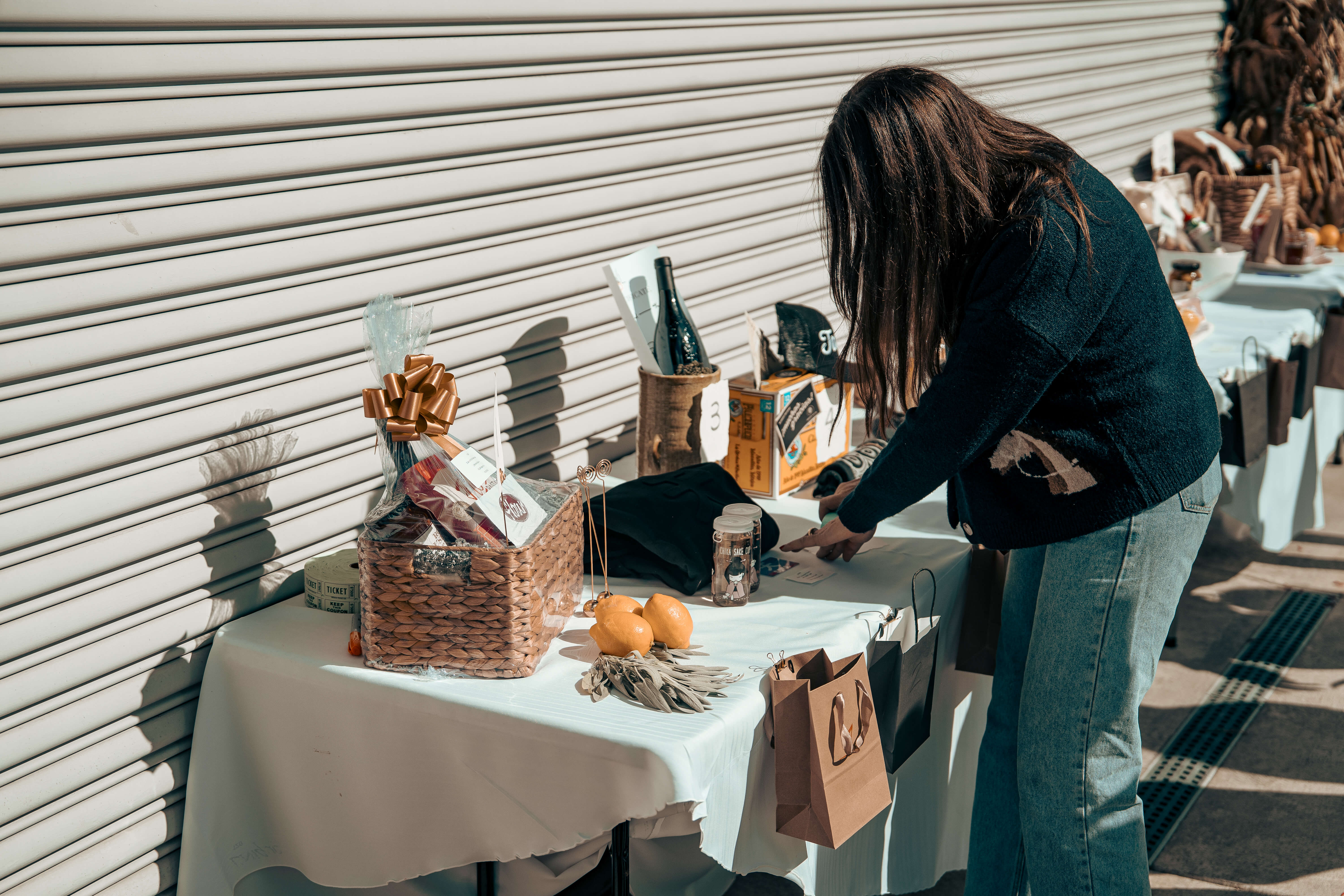 Person arranging gift basket with wine, oranges, and wrapped presents