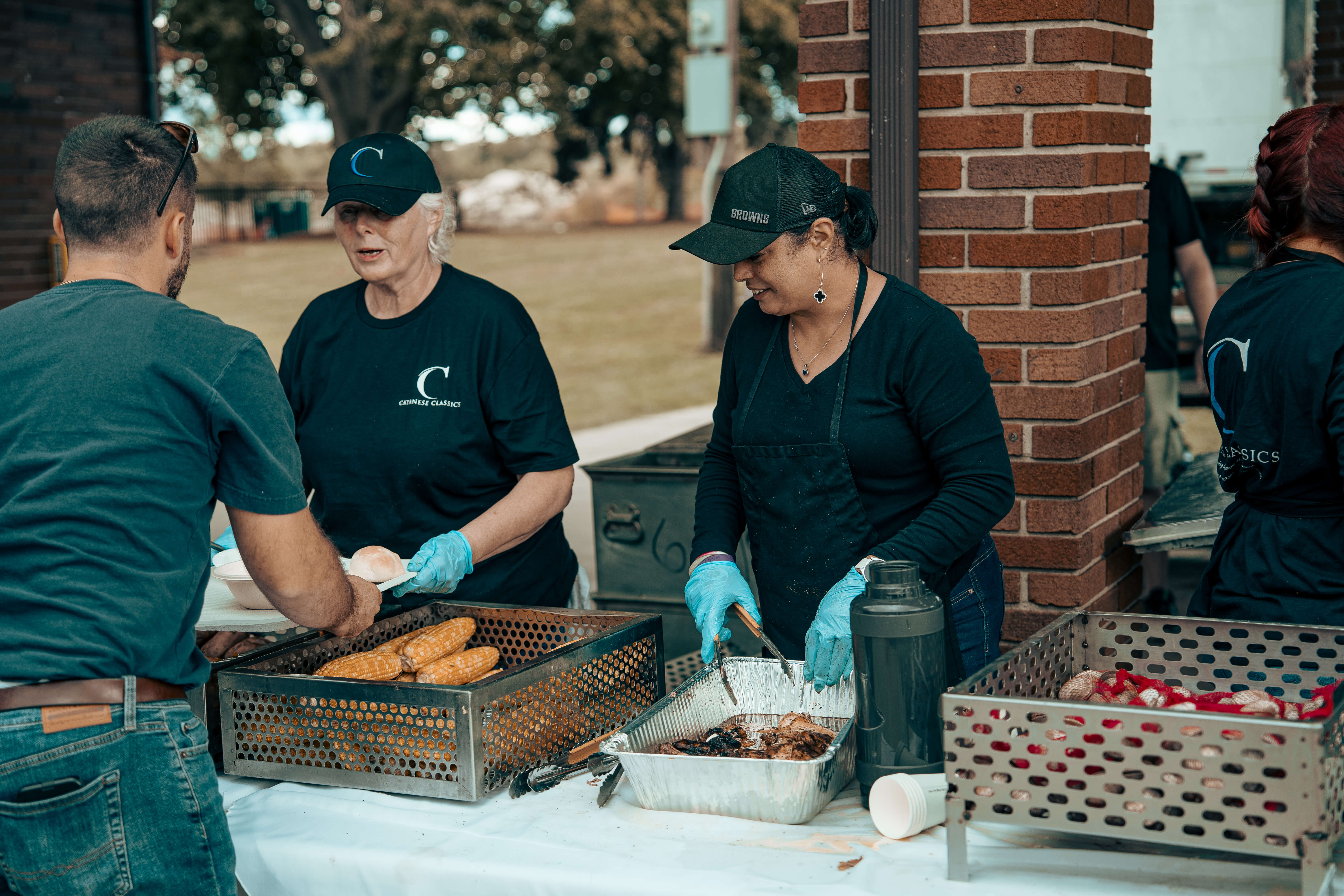 Volunteers serving food at outdoor event wearing matching shirts and caps