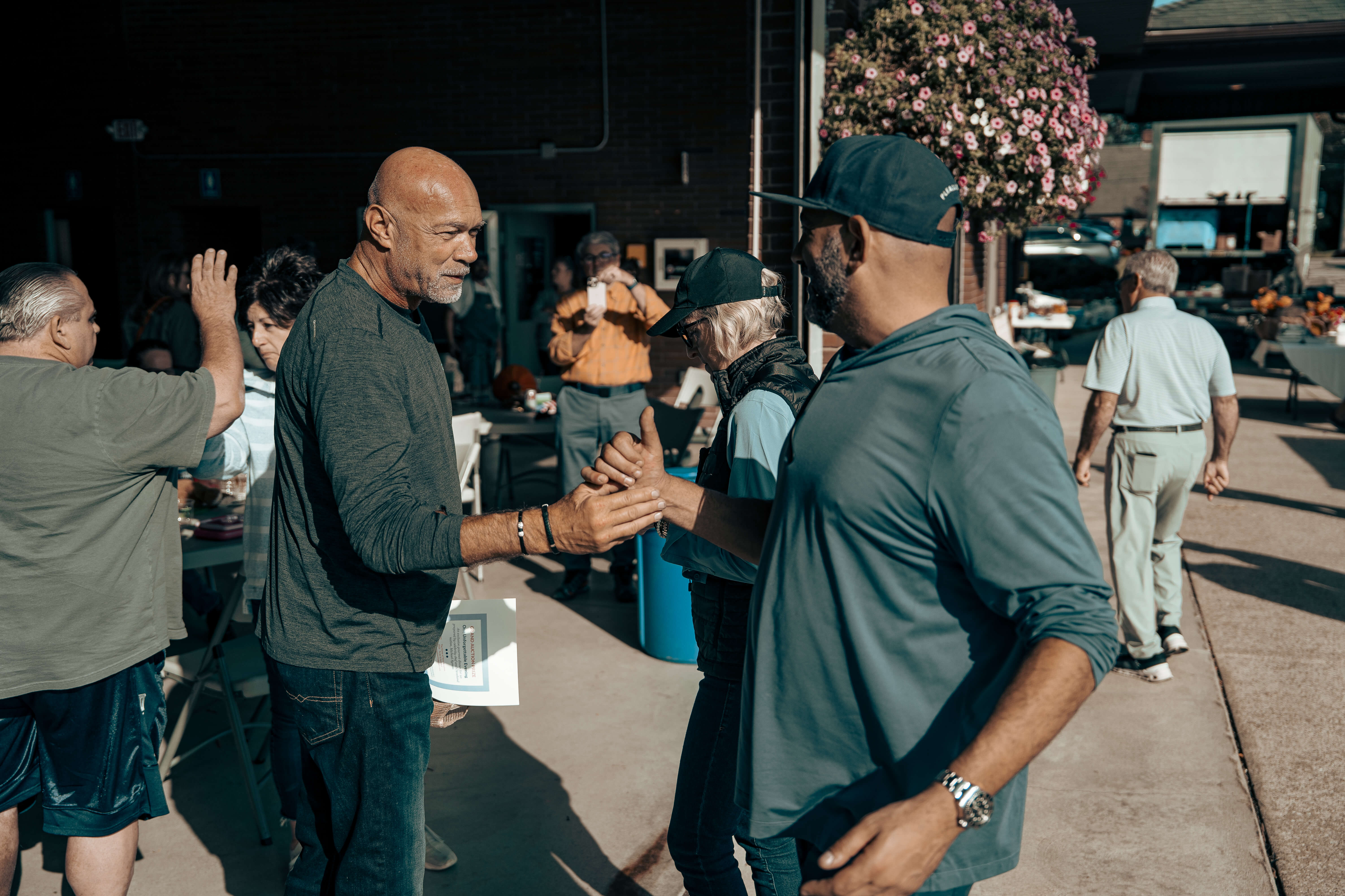 Men greeting each other on sunny outdoor patio with flowering plant