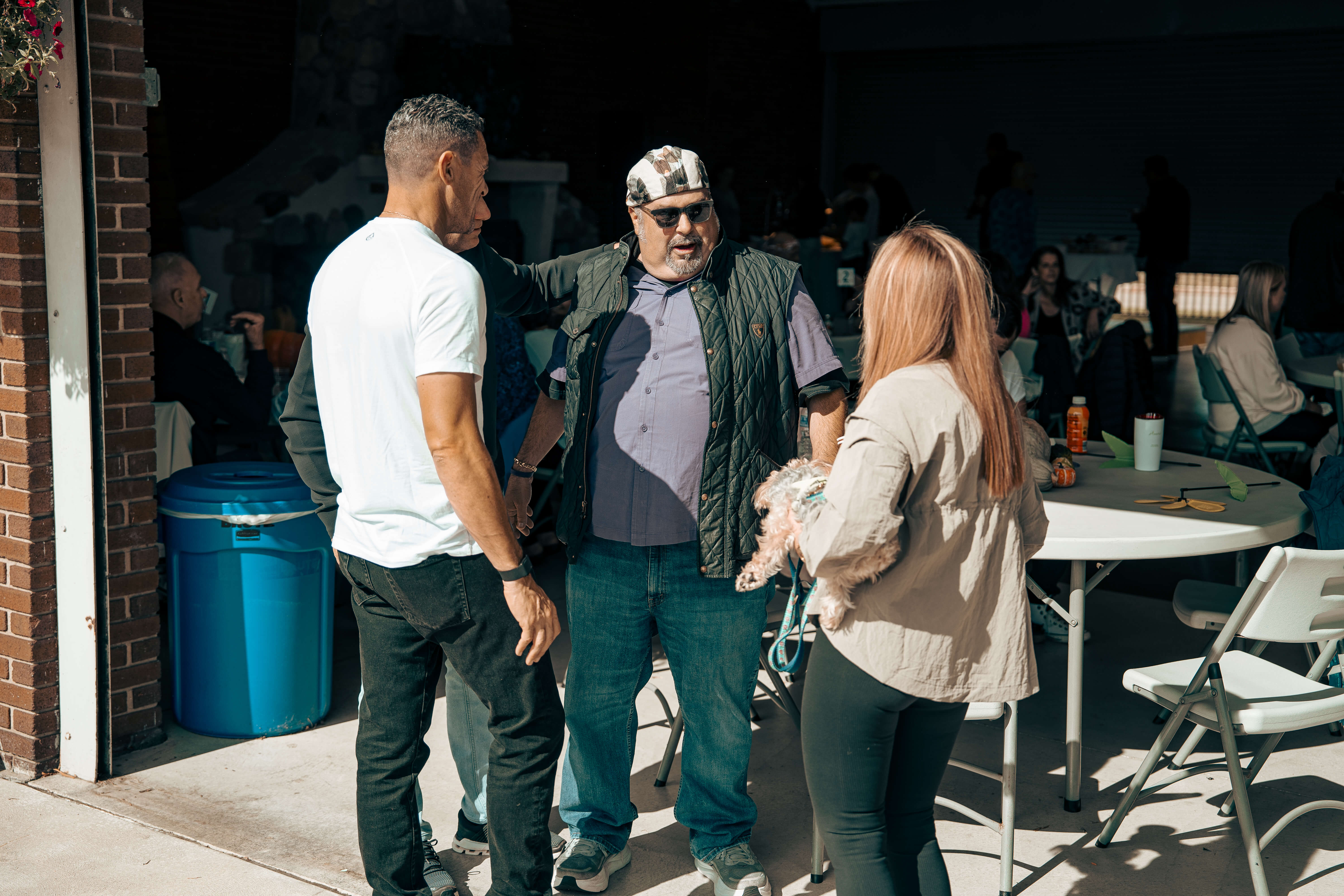 Three people talking near blue barrel, one holding small dog