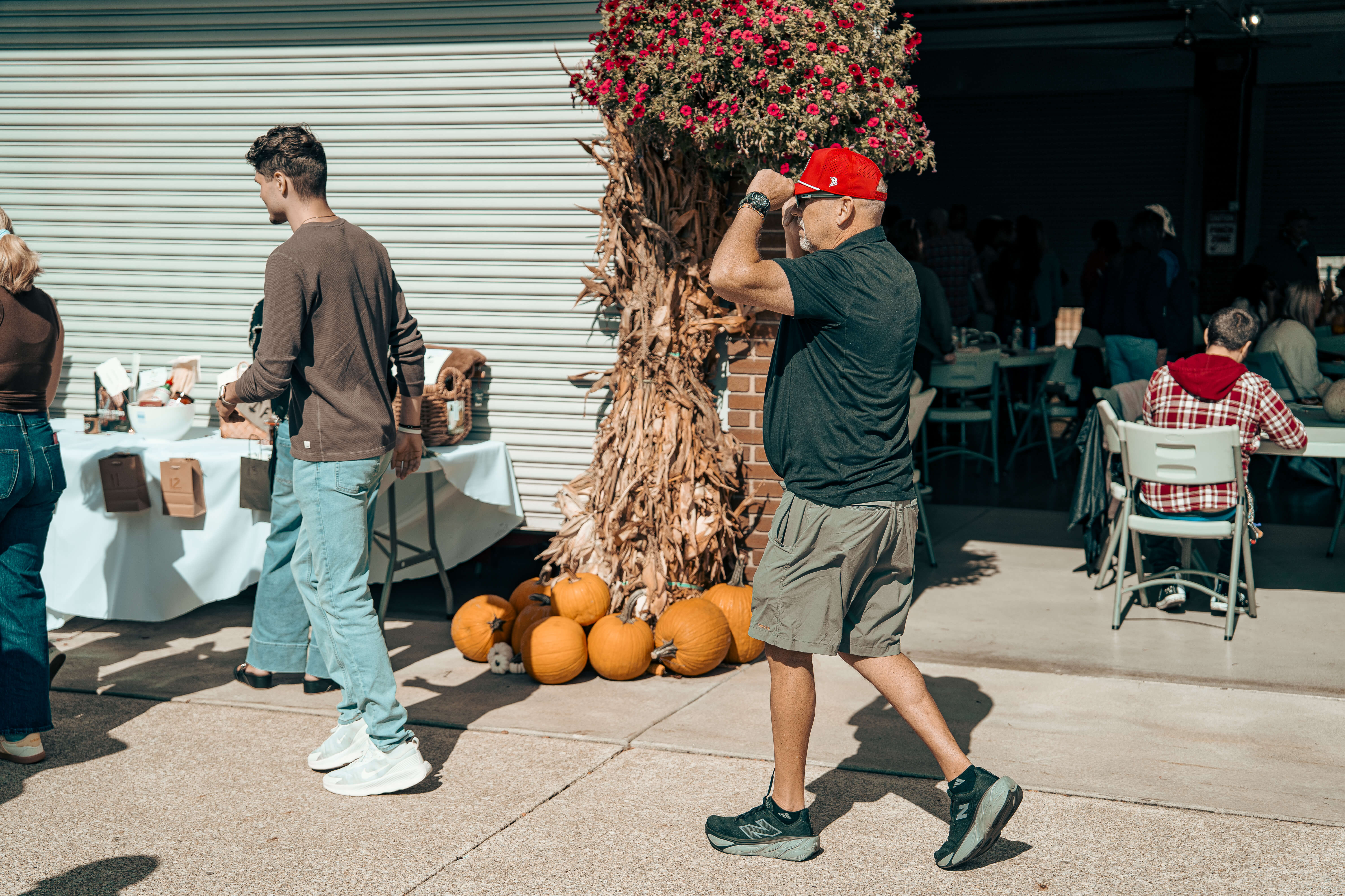 Outdoor scene with pumpkins, white tables, and people near flowering tree