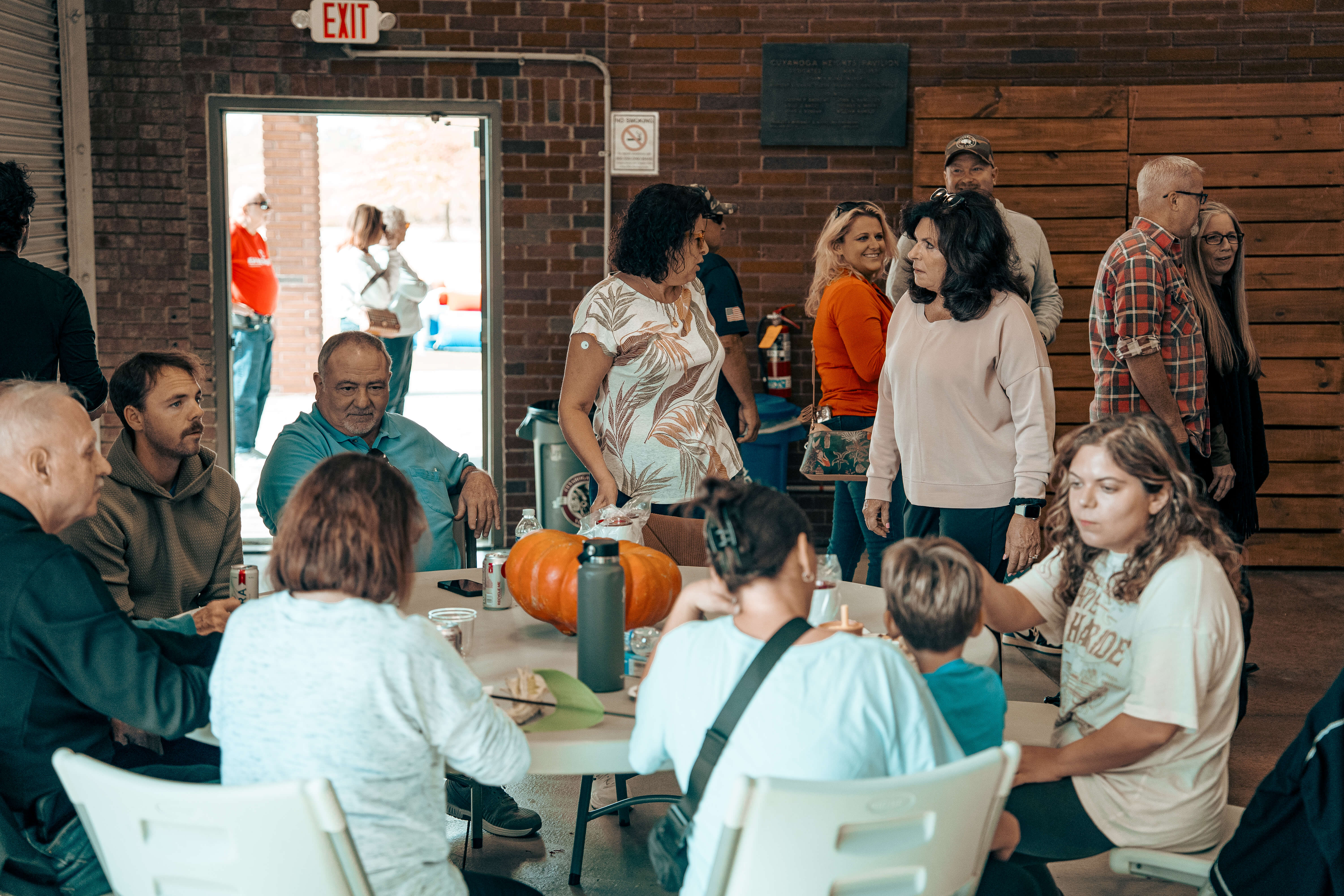 Group gathered around a table with a large pumpkin, brick interior