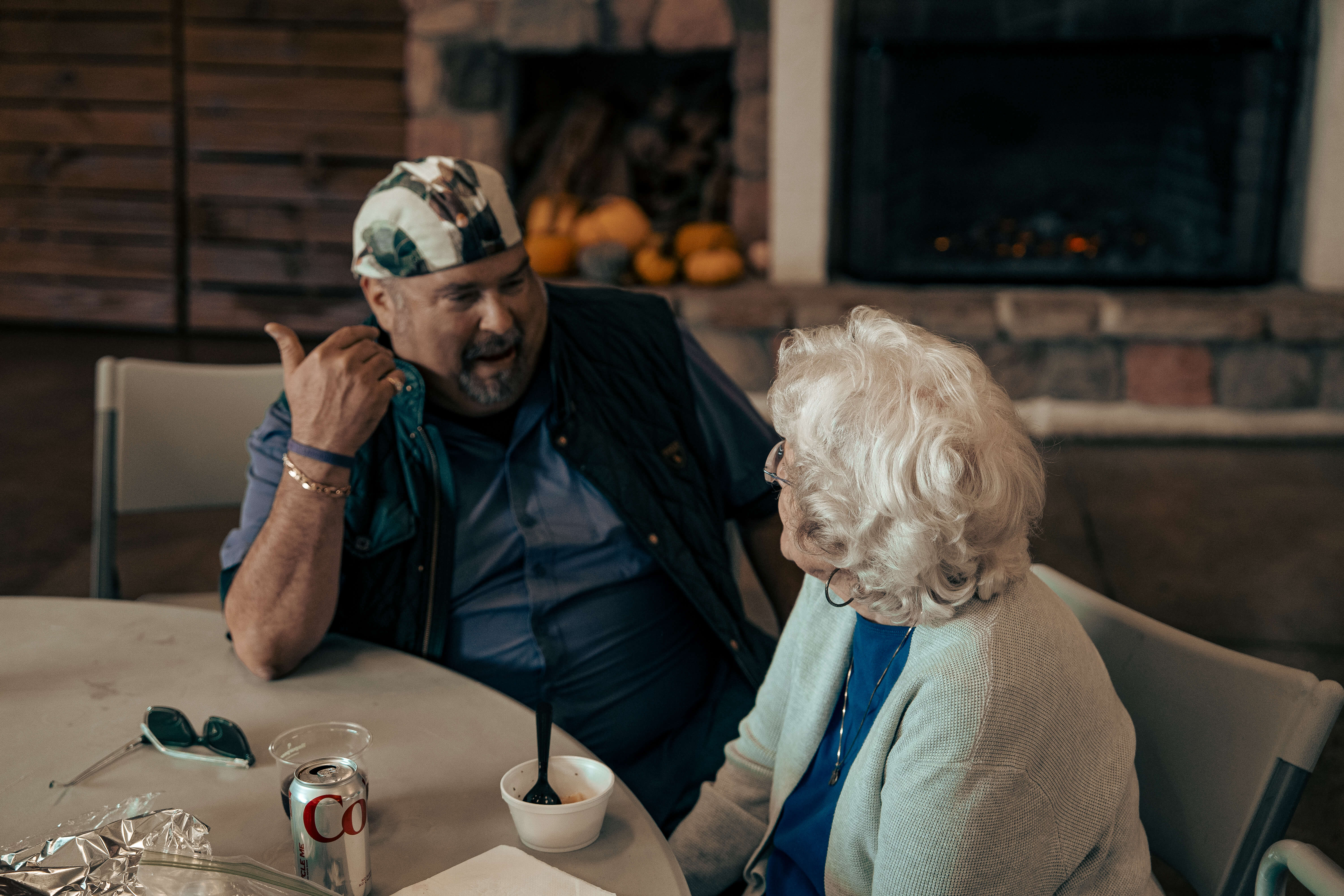 Two seniors chatting and enjoying a drink by a cozy fireplace