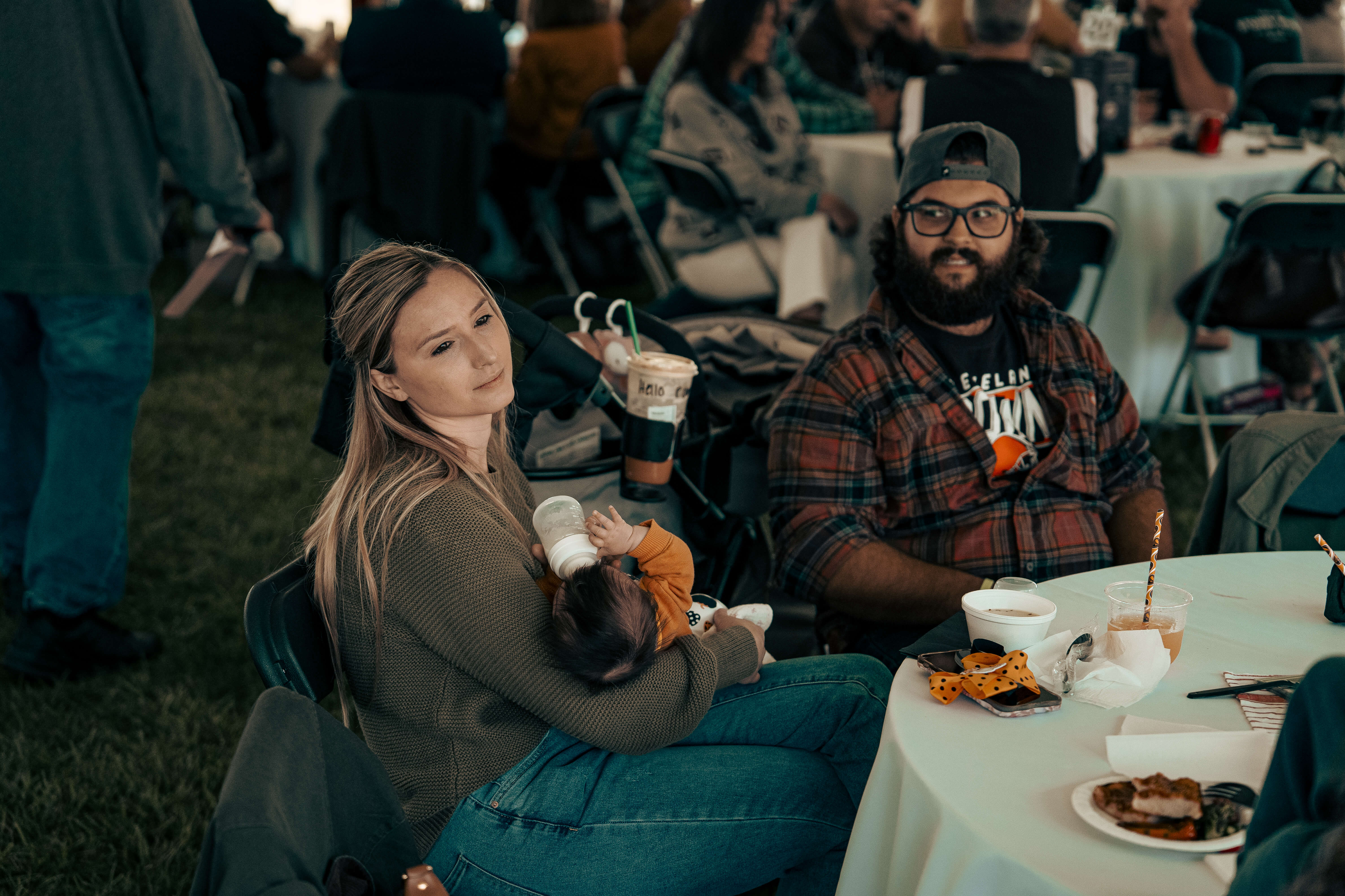 Woman feeding baby at outdoor event with bearded man nearby