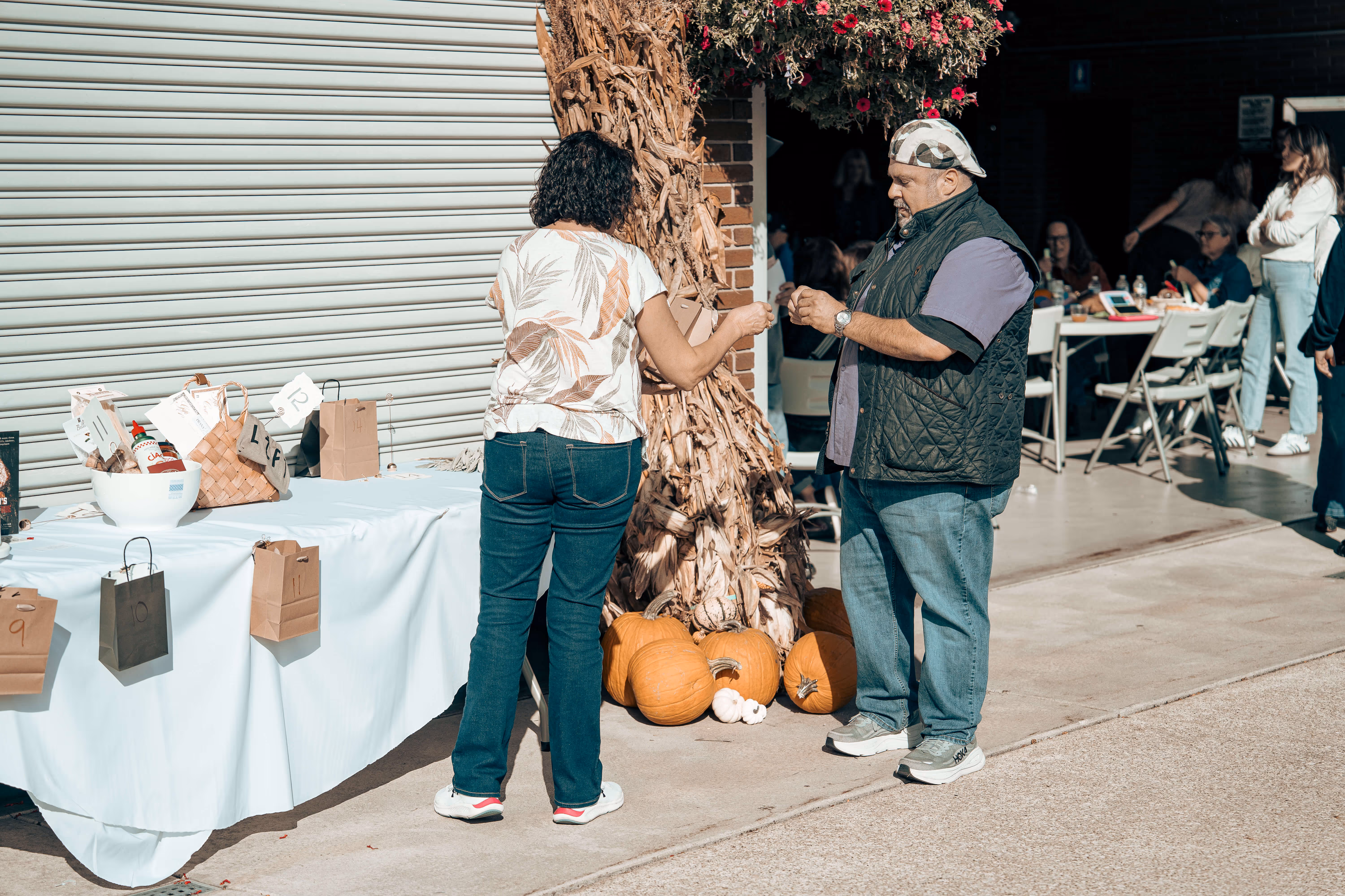 Two people near pumpkins and gift bags at an outdoor fall market event
