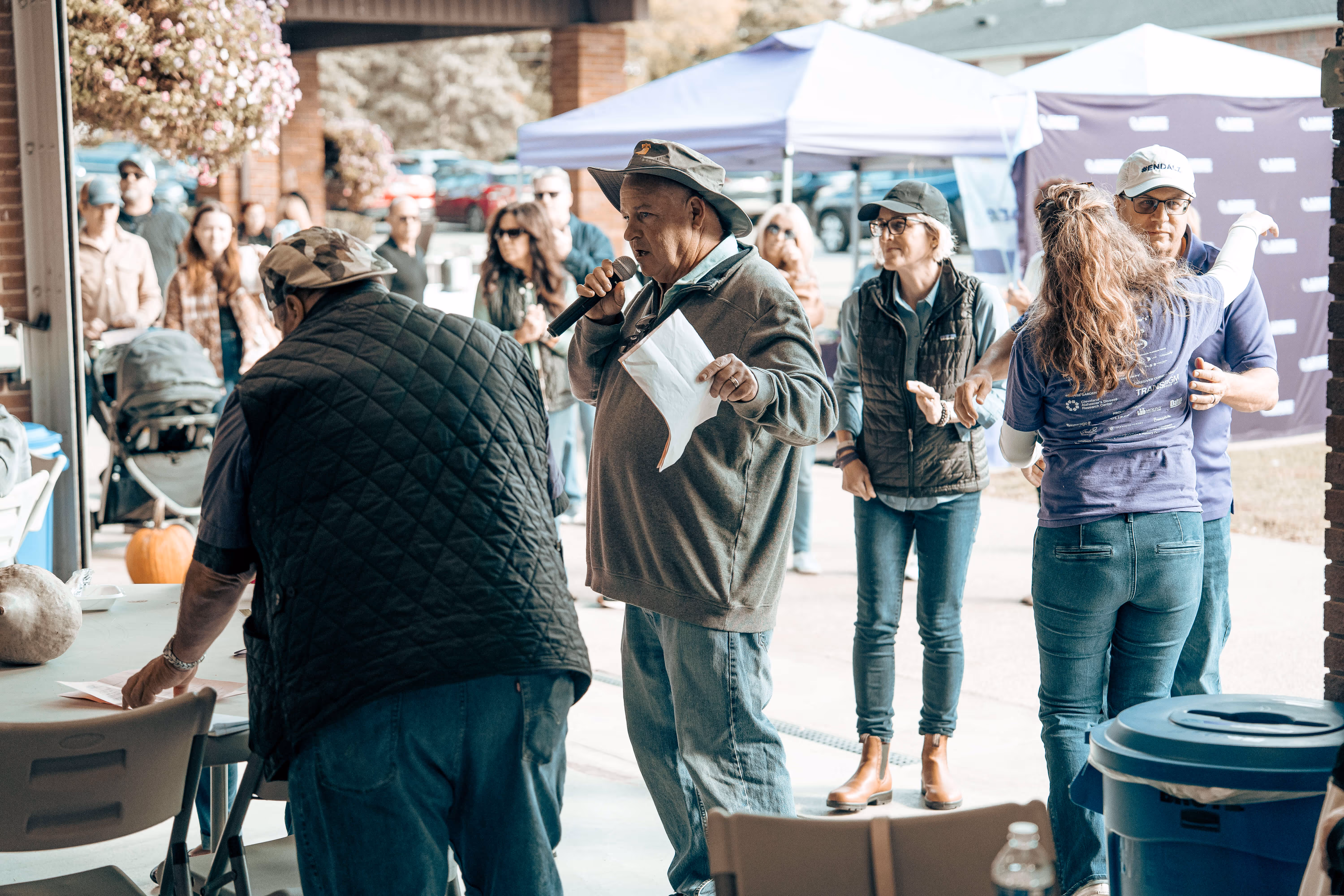 Outdoor event with speaker at microphone, people listening in background