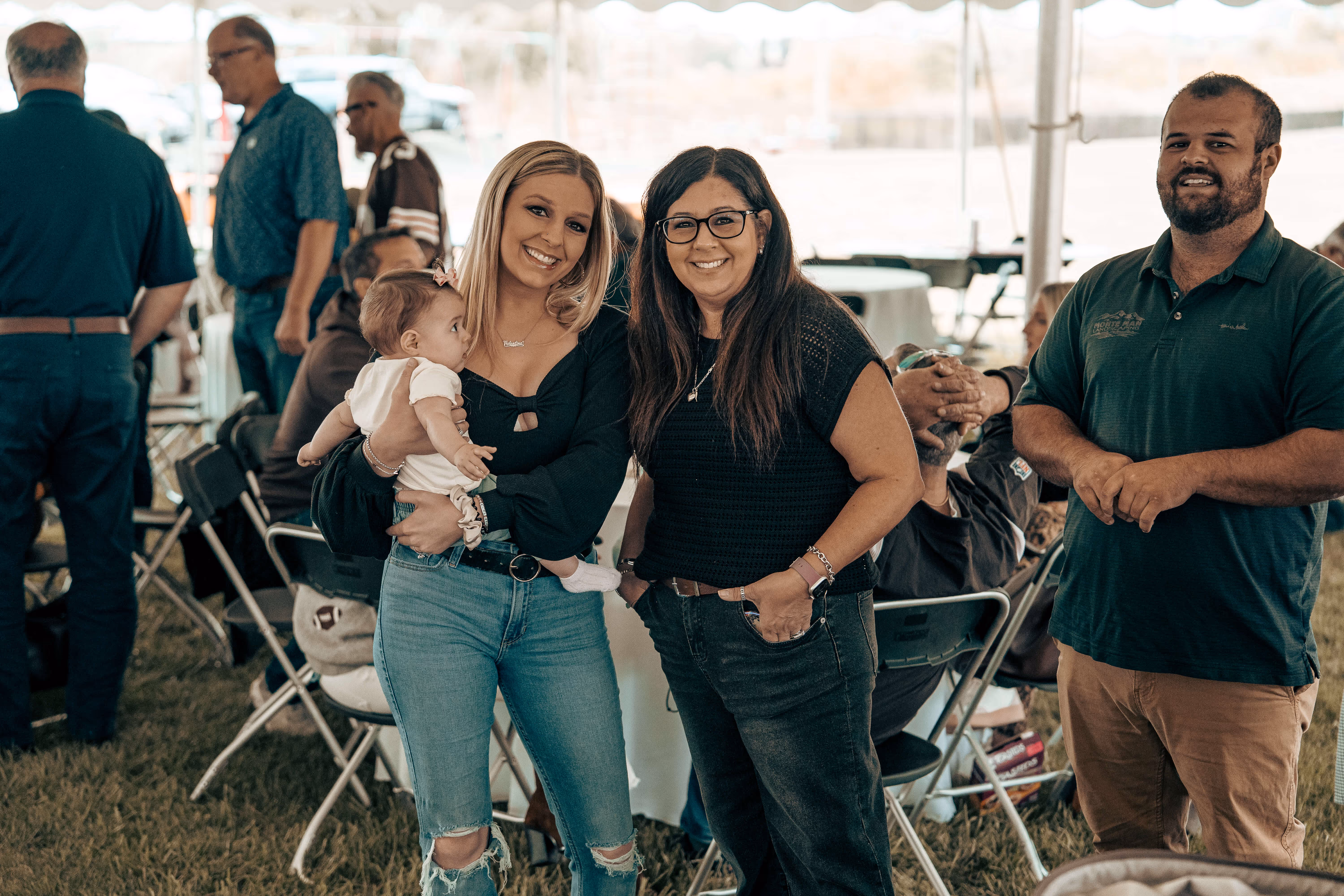 Smiling women with baby and man at outdoor event with folding chairs