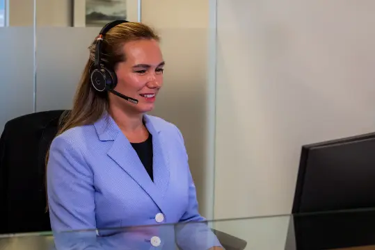 Smiling customer service representative wearing a headset and a blue blazer, providing friendly support at a computer workstation.